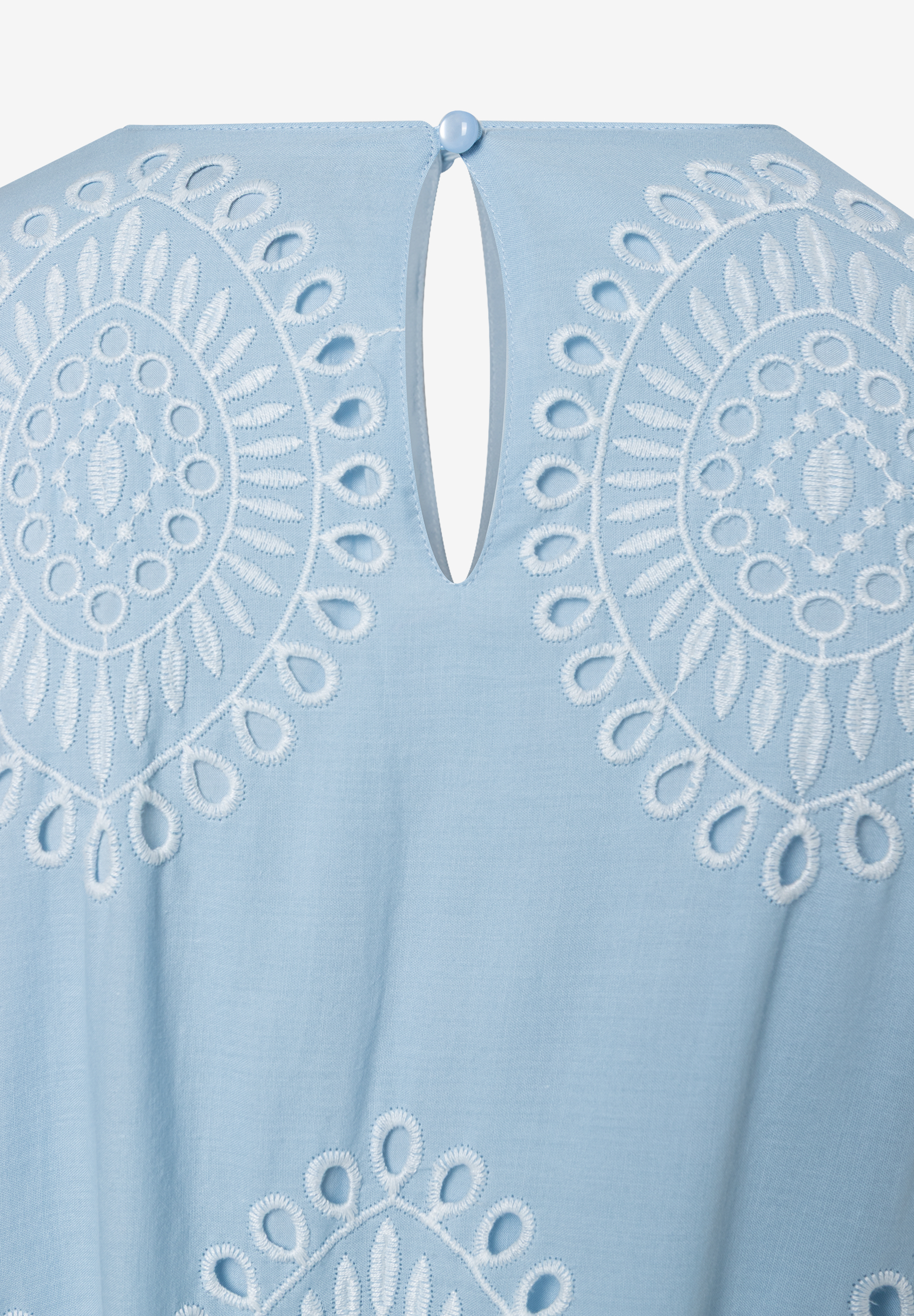 Ein hellblaues MORE & MORE Oberteil mit weißer Lochstickerei und Knopfdetail am Nacken. Ein hellblaues MORE & MORE Oberteil mit weißer Lochstickerei und Knopfdetail am Nacken.
