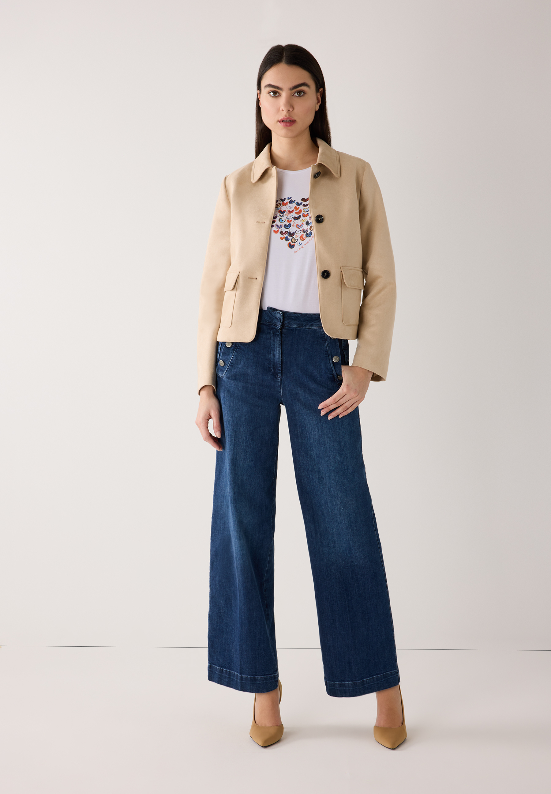 Eine Frau in MORE & MORE Oberteilen, Jeans und hellbraunen Schuhen vor hellem Hintergrund. Eine Frau in MORE & MORE Oberteilen, Jeans und hellbraunen Schuhen vor hellem Hintergrund.