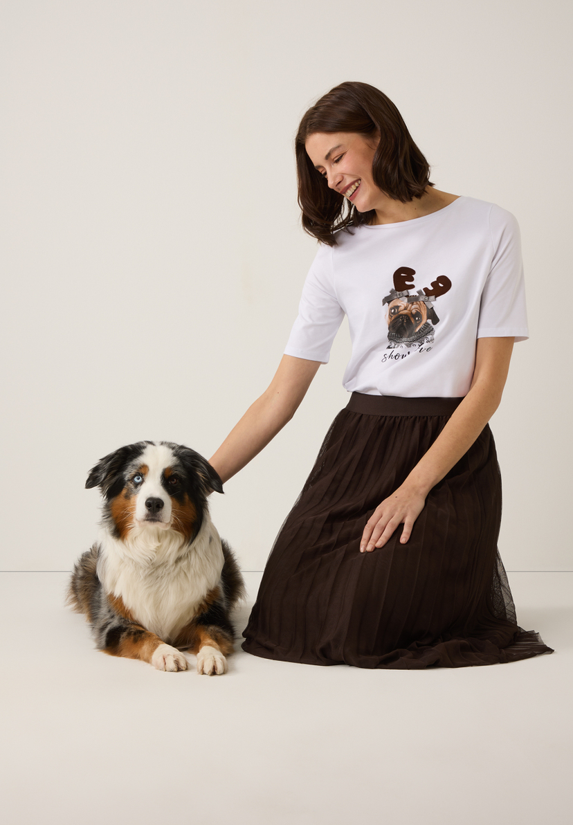Eine Frau streichelt einen Hund. Sie trägt ein MORE & MORE-Top mit einem Mops mit Geweih. Jersey-Material für angenehmen Tragekomfort. Eine Frau streichelt einen Hund. Sie trägt ein MORE & MORE-Top mit einem Mops mit Geweih. Jersey-Material für angenehmen Tragekomfort.