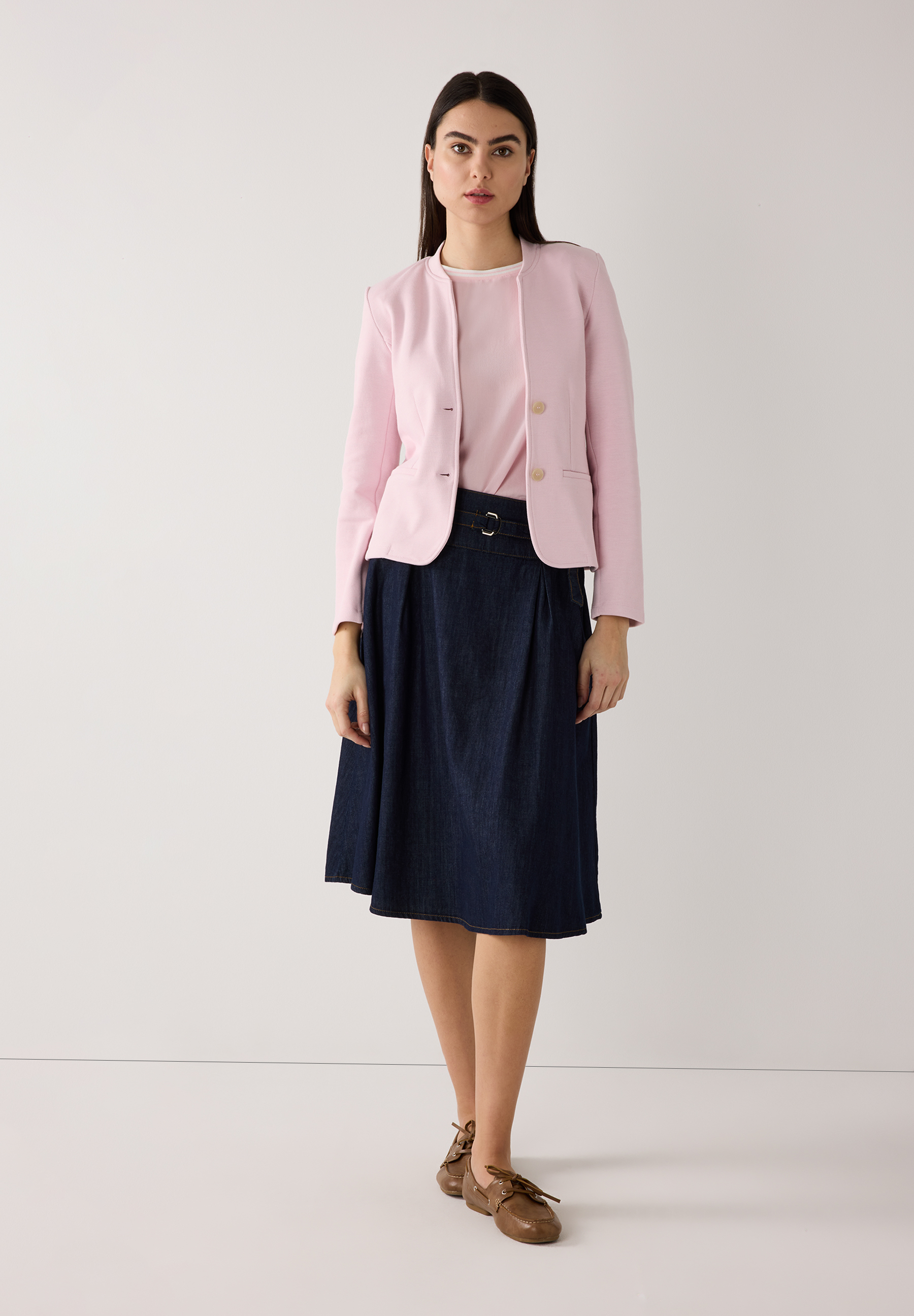 Eine Frau trägt einen MORE & MORE Blazer in Rosa, ein passendes Shirt und einen Jeansrock vor einem neutralen Hintergrund. Eine Frau trägt einen MORE & MORE Blazer in Rosa, ein passendes Shirt und einen Jeansrock vor einem neutralen Hintergrund.