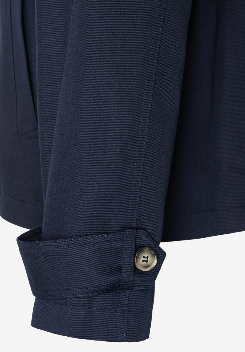 Detailaufnahme einer marineblauen MORE & MORE Jacke aus Twill mit Knopf am Ärmel und einer Tasche. Detailaufnahme einer marineblauen MORE & MORE Jacke aus Twill mit Knopf am Ärmel und einer Tasche.