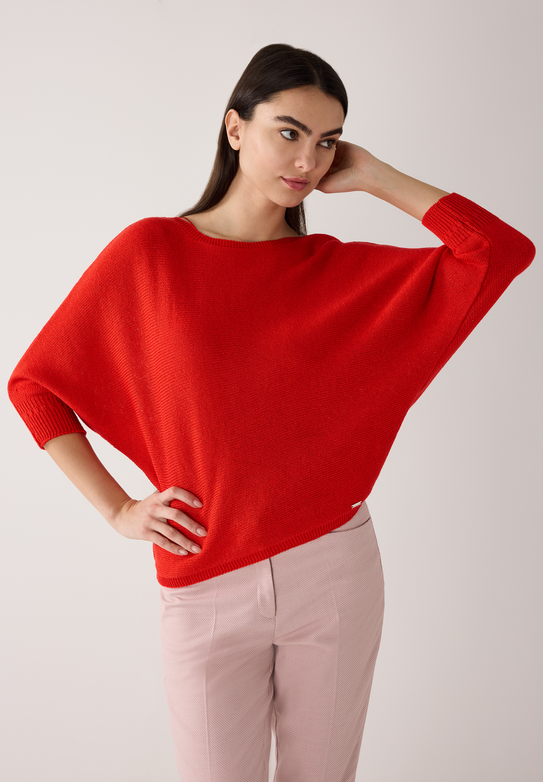 Eine Frau trägt einen roten Strick-Pullover von MORE & MORE und rosafarbene Hosen vor einem hellen Hintergrund. Eine Frau trägt einen roten Strick-Pullover von MORE & MORE und rosafarbene Hosen vor einem hellen Hintergrund.