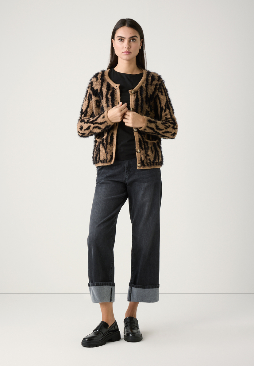 Eine Frau in MORE & MORE Strick-Oberteilen, dunklen Jeans und schwarzen Schuhen vor einem weißen Hintergrund. Eine Frau in MORE & MORE Strick-Oberteilen, dunklen Jeans und schwarzen Schuhen vor einem weißen Hintergrund.