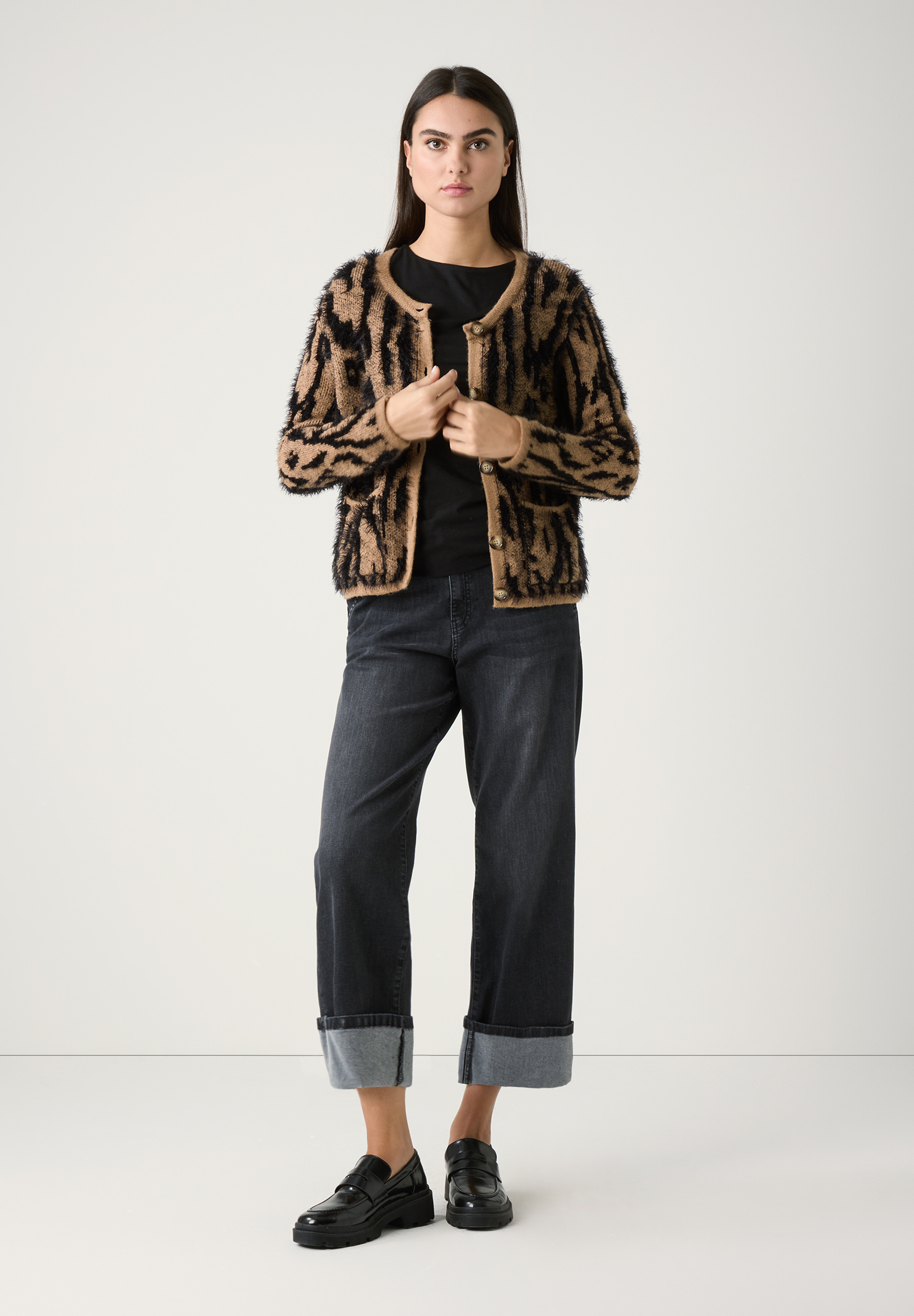 Eine Frau in MORE & MORE Strick-Oberteilen, dunklen Jeans und schwarzen Schuhen vor einem weißen Hintergrund. Eine Frau in MORE & MORE Strick-Oberteilen, dunklen Jeans und schwarzen Schuhen vor einem weißen Hintergrund.