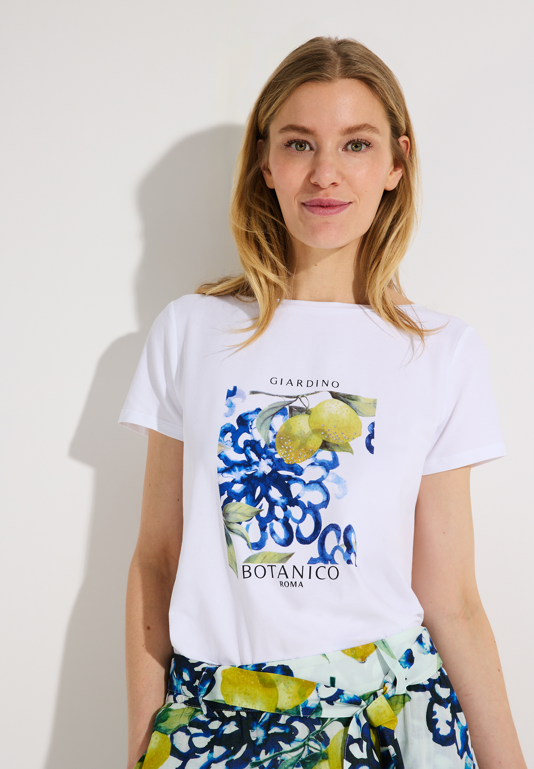 Eine Frau trägt ein weißes MORE & MORE T-Shirt mit einem Blumen- und Zitronenmotiv.