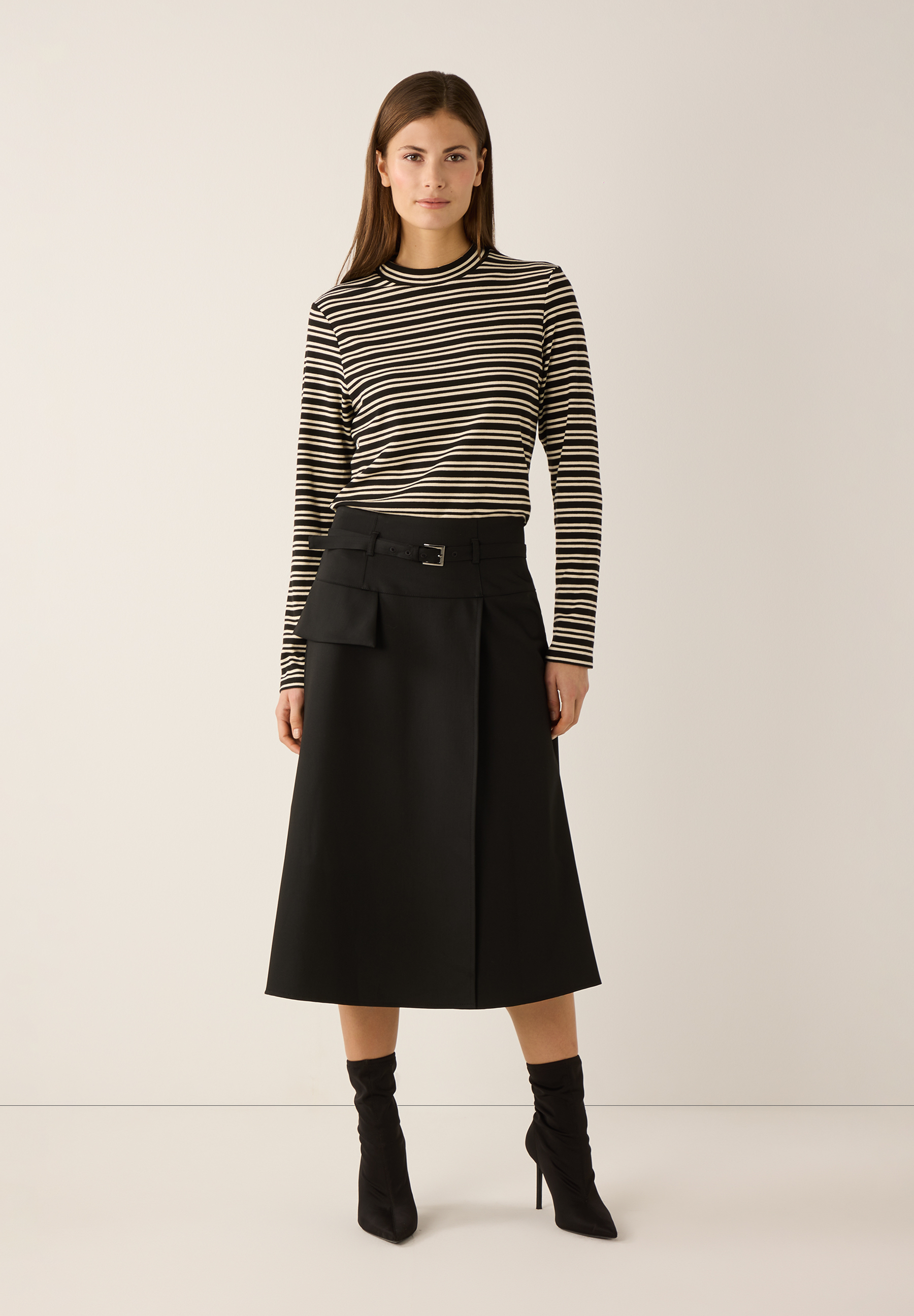 Eine Frau zeigt einen schwarzen MORE & MORE Rock mit Gürtel und Seitentasche. Eine Frau zeigt einen schwarzen MORE & MORE Rock mit Gürtel und Seitentasche.