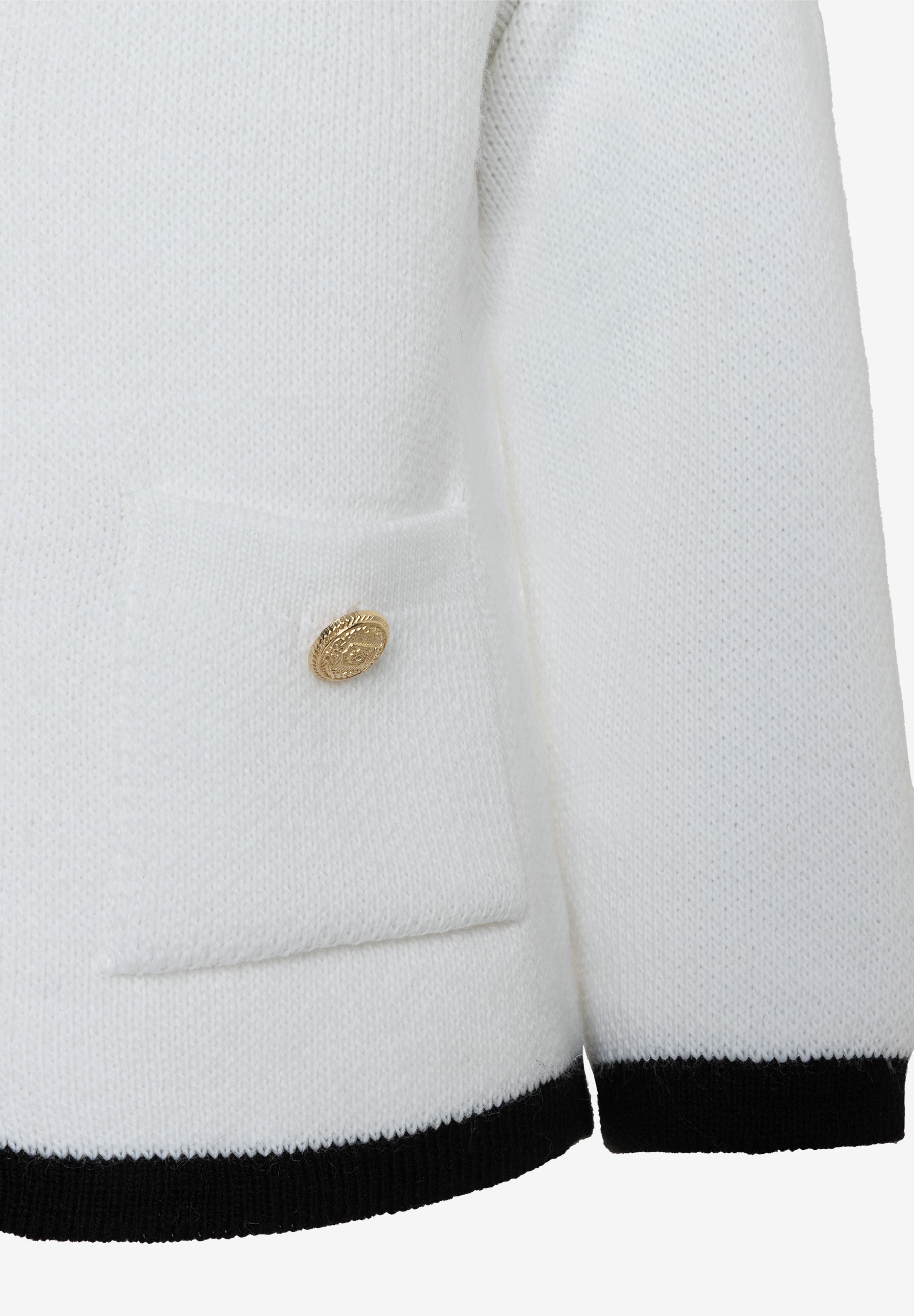 Nahaufnahme eines weißen MORE & MORE Strickpullovers mit goldfarbenem Knopf an der Tasche und schwarzem Saum. Nahaufnahme eines weißen MORE & MORE Strickpullovers mit goldfarbenem Knopf an der Tasche und schwarzem Saum.