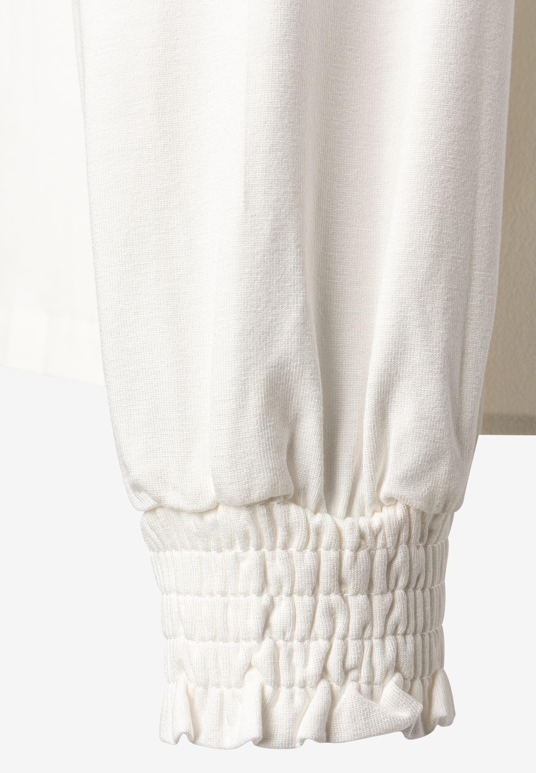 MORE & MORE Bluse: Detailaufnahme des gekräuselten, gerüschten Ärmelbunds einer cremeweißen Bluse. MORE & MORE Bluse: Detailaufnahme des gekräuselten, gerüschten Ärmelbunds einer cremeweißen Bluse.
