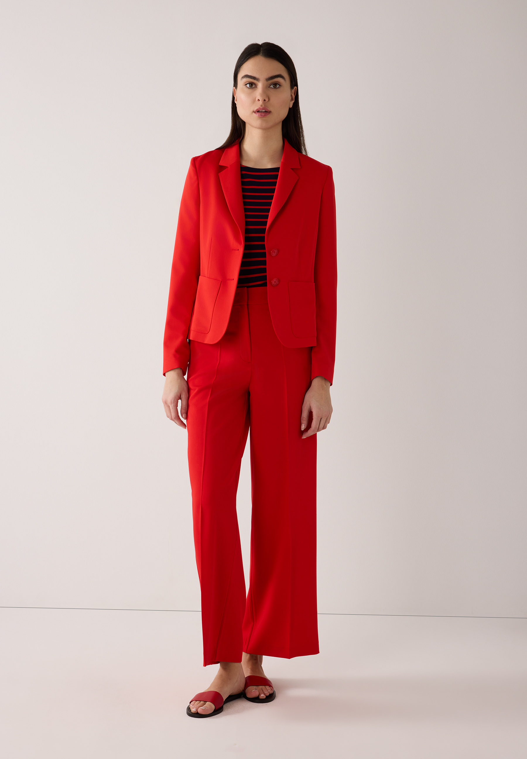 Eine Frau in einem roten MORE & MORE Blazer und einer passenden Hose, dazu ein gestreiftes Oberteil. Eine Frau in einem roten MORE & MORE Blazer und einer passenden Hose, dazu ein gestreiftes Oberteil.