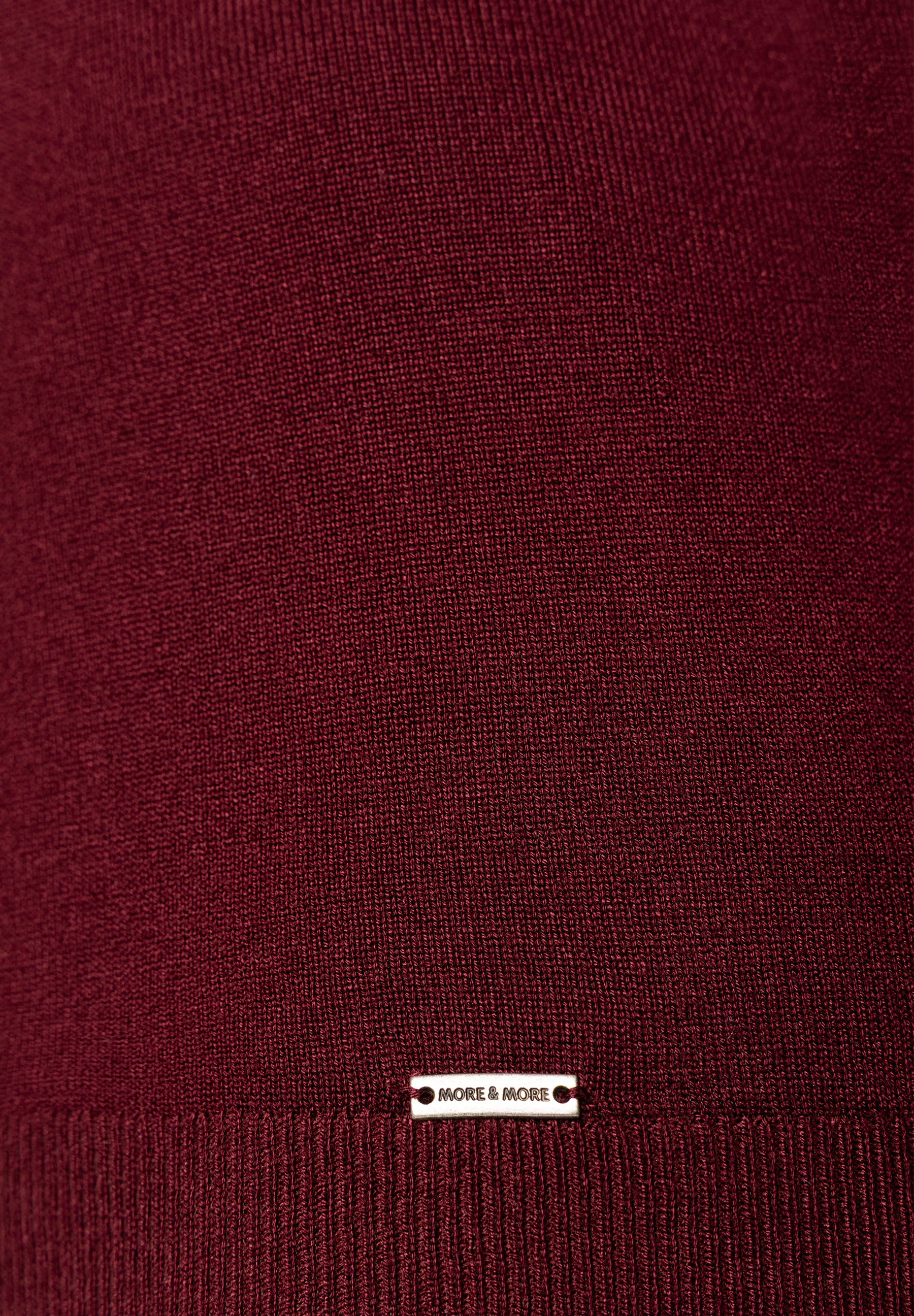 MORE & MORE dunkelroter Feinstrickpullover, Nahaufnahme des Saums mit Logoplakette. Strukturierter Strickstoff. MORE & MORE dunkelroter Feinstrickpullover, Nahaufnahme des Saums mit Logoplakette. Strukturierter Strickstoff.