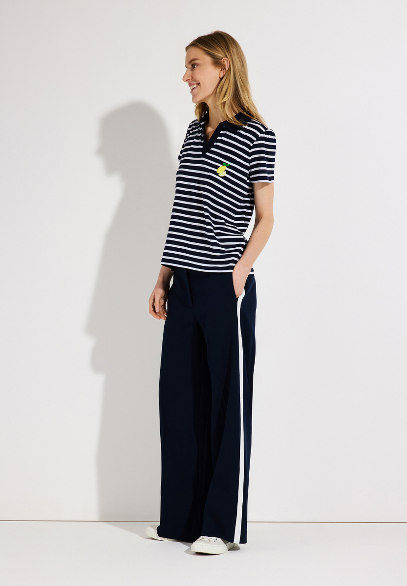 Eine Frau trägt ein gestreiftes MORE & MORE Jersey-Top mit einer kleinen Zitrone und eine dunkelblaue Hose mit weißem Streifen. Eine Frau trägt ein gestreiftes MORE & MORE Jersey-Top mit einer kleinen Zitrone und eine dunkelblaue Hose mit weißem Streifen.