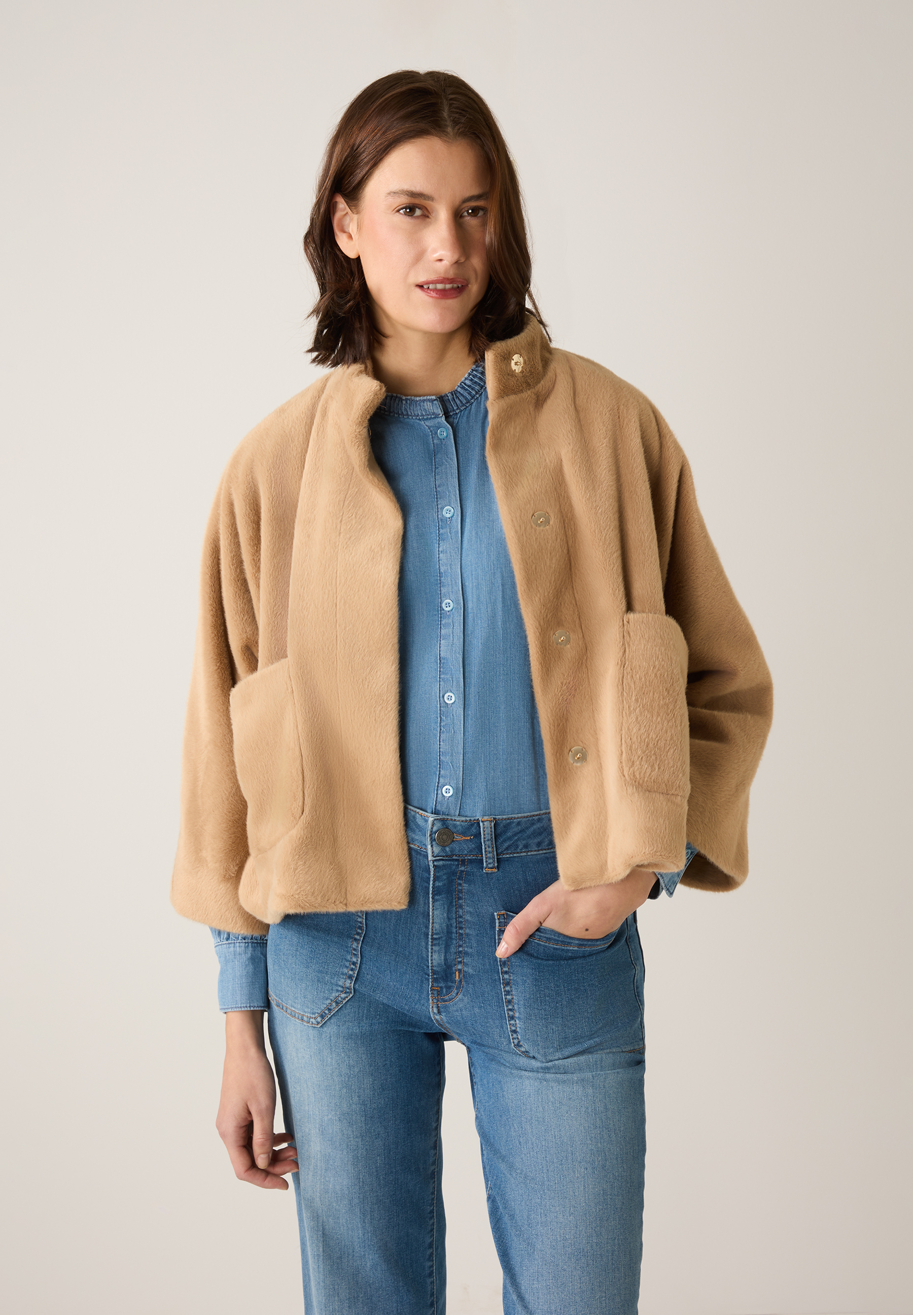 Eine Frau trägt eine warme MORE & MORE Jacke aus Kunstfell über einem Jeanshemd und einer Jeans. Eine Frau trägt eine warme MORE & MORE Jacke aus Kunstfell über einem Jeanshemd und einer Jeans.