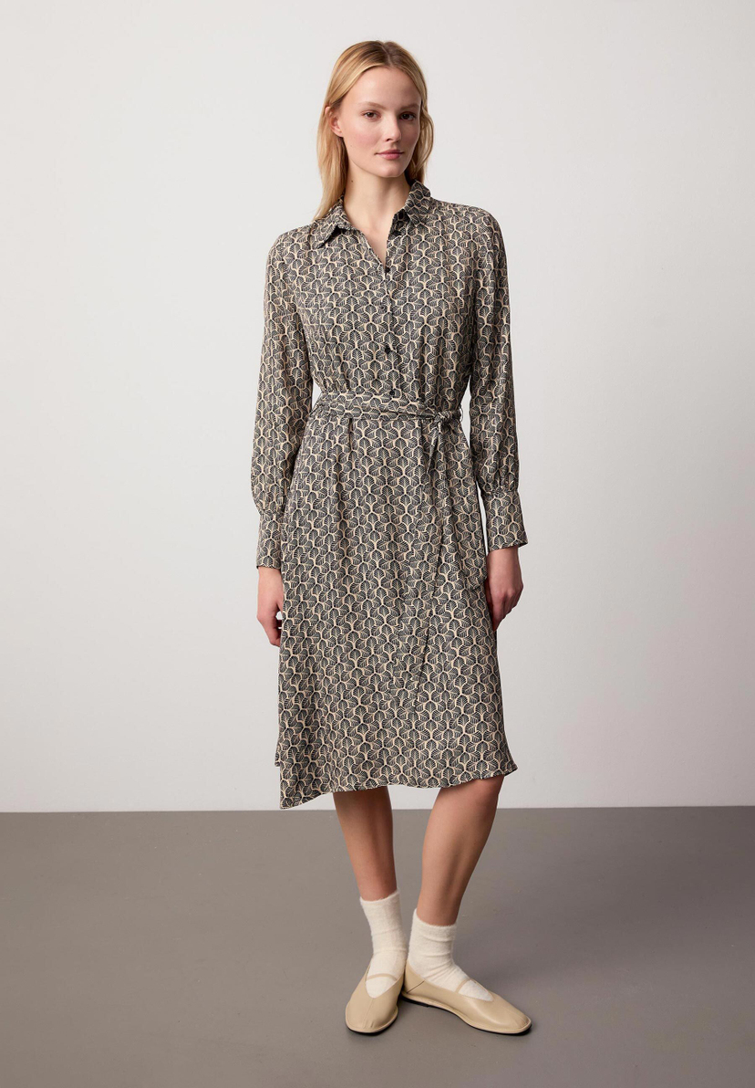 Eine blonde Frau zeigt ein gemustertes, tailliertes Hemdblusenkleid von MORE & MORE mit langen Ärmeln. Eine blonde Frau zeigt ein gemustertes, tailliertes Hemdblusenkleid von MORE & MORE mit langen Ärmeln.