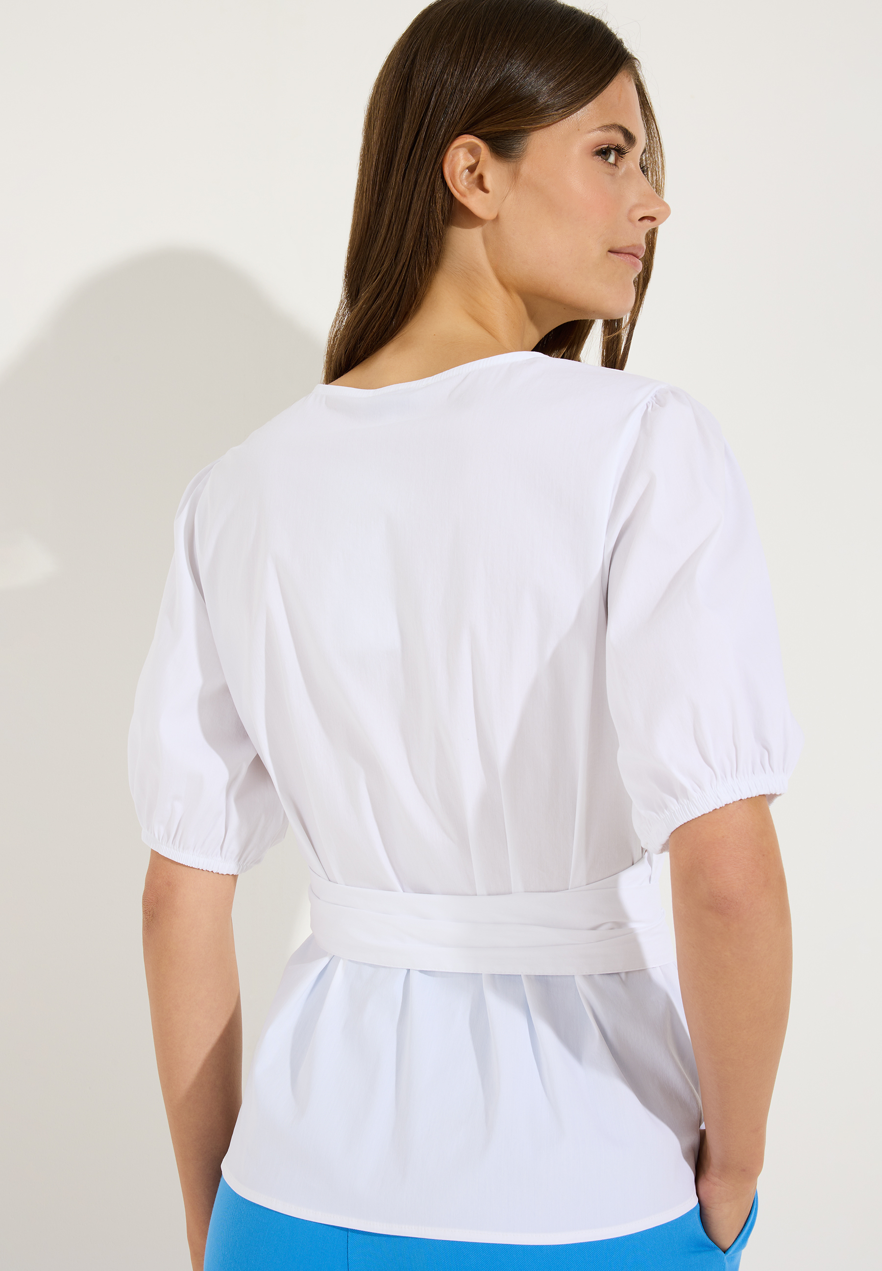 MORE & MORE Bluse: Eine Frau von hinten trägt eine weiße Bluse mit Gürtel und hellblauer Hose. Das Haar der Frau ist lang und braun. MORE & MORE Bluse: Eine Frau von hinten trägt eine weiße Bluse mit Gürtel und hellblauer Hose. Das Haar der Frau ist lang und braun.