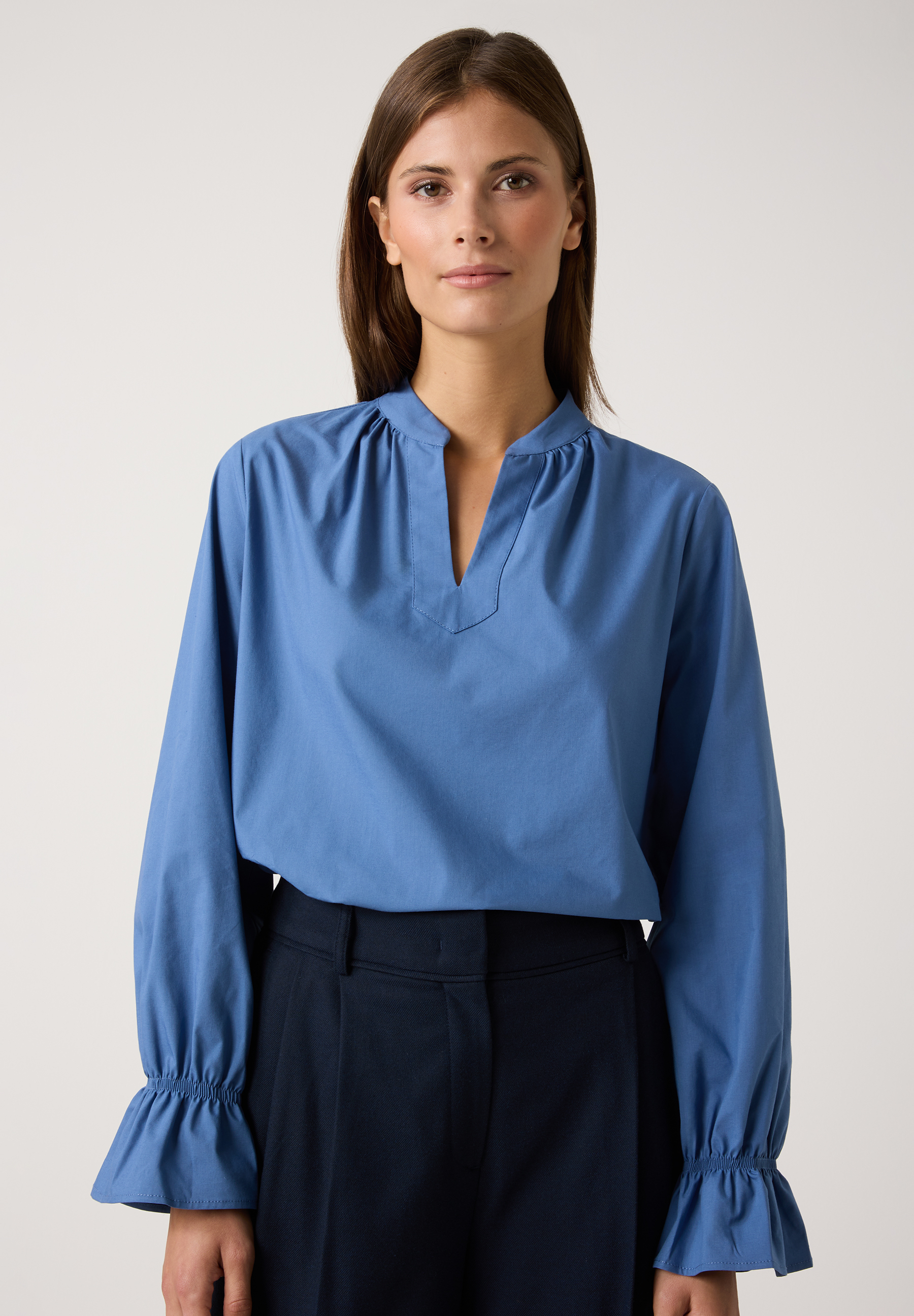 Eine Frau, die eine blaue MORE & MORE Bluse und eine dunkle Hose trägt.