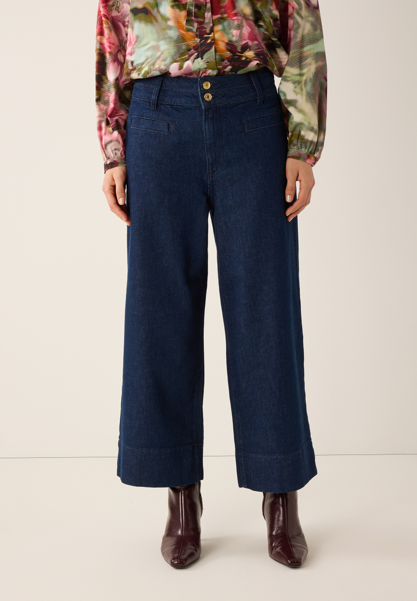 Eine Frau mit MORE & MORE Jeans und floraler Bluse steht vor einem neutralen Hintergrund. Eine Frau mit MORE & MORE Jeans und floraler Bluse steht vor einem neutralen Hintergrund.