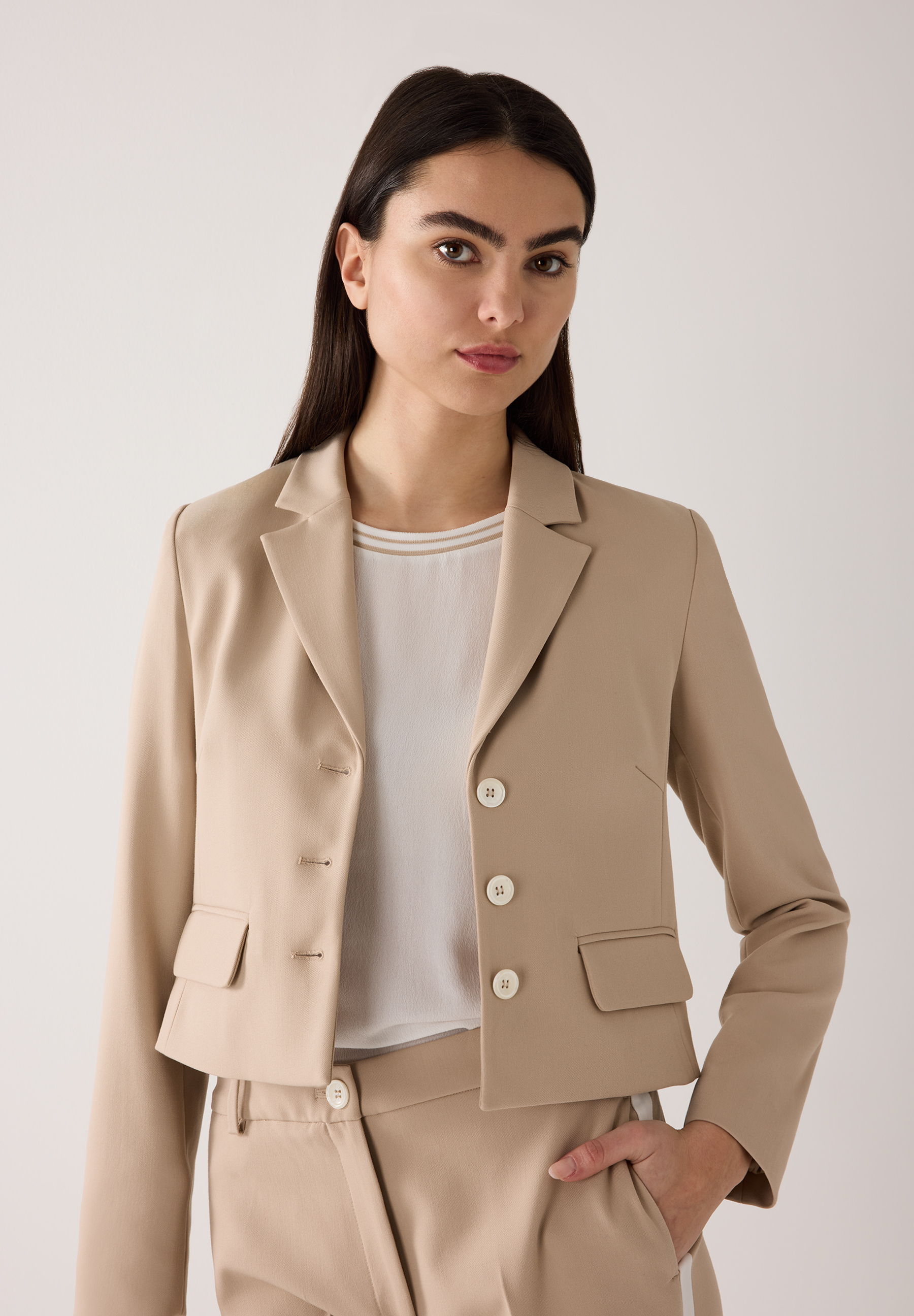 Eine Frau trägt einen hellbraunen Blazer von MORE & MORE mit weißen Knöpfen.