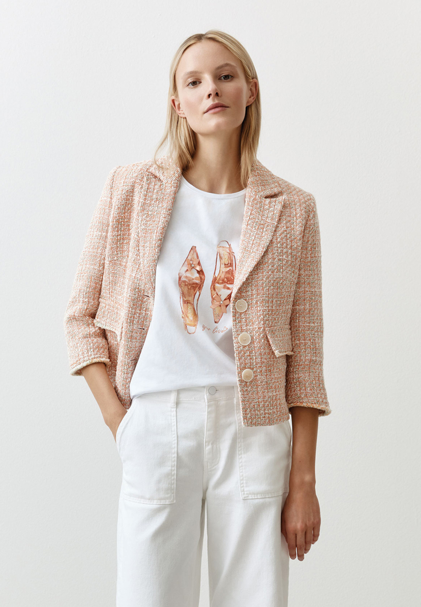 Eine Frau mit blonden, schulterlangen Haaren trägt einen formstabilen Bouclé-Blazer von MORE & MORE, ein T-Shirt und weiße Hosen. Eine Frau mit blonden, schulterlangen Haaren trägt einen formstabilen Bouclé-Blazer von MORE & MORE, ein T-Shirt und weiße Hosen.