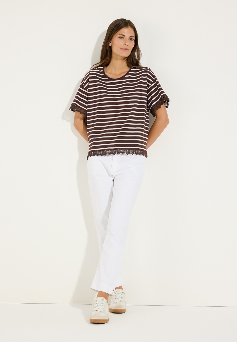 MORE & MORE Damen-Jersey-Shirt gestreift, mit Spitze an Ärmeln und Saum, in Braun/Weiß. Die Frau trägt dazu weiße Hosen und beigefarbene Sneaker. MORE & MORE Damen-Jersey-Shirt gestreift, mit Spitze an Ärmeln und Saum, in Braun/Weiß. Die Frau trägt dazu weiße Hosen und beigefarbene Sneaker.
