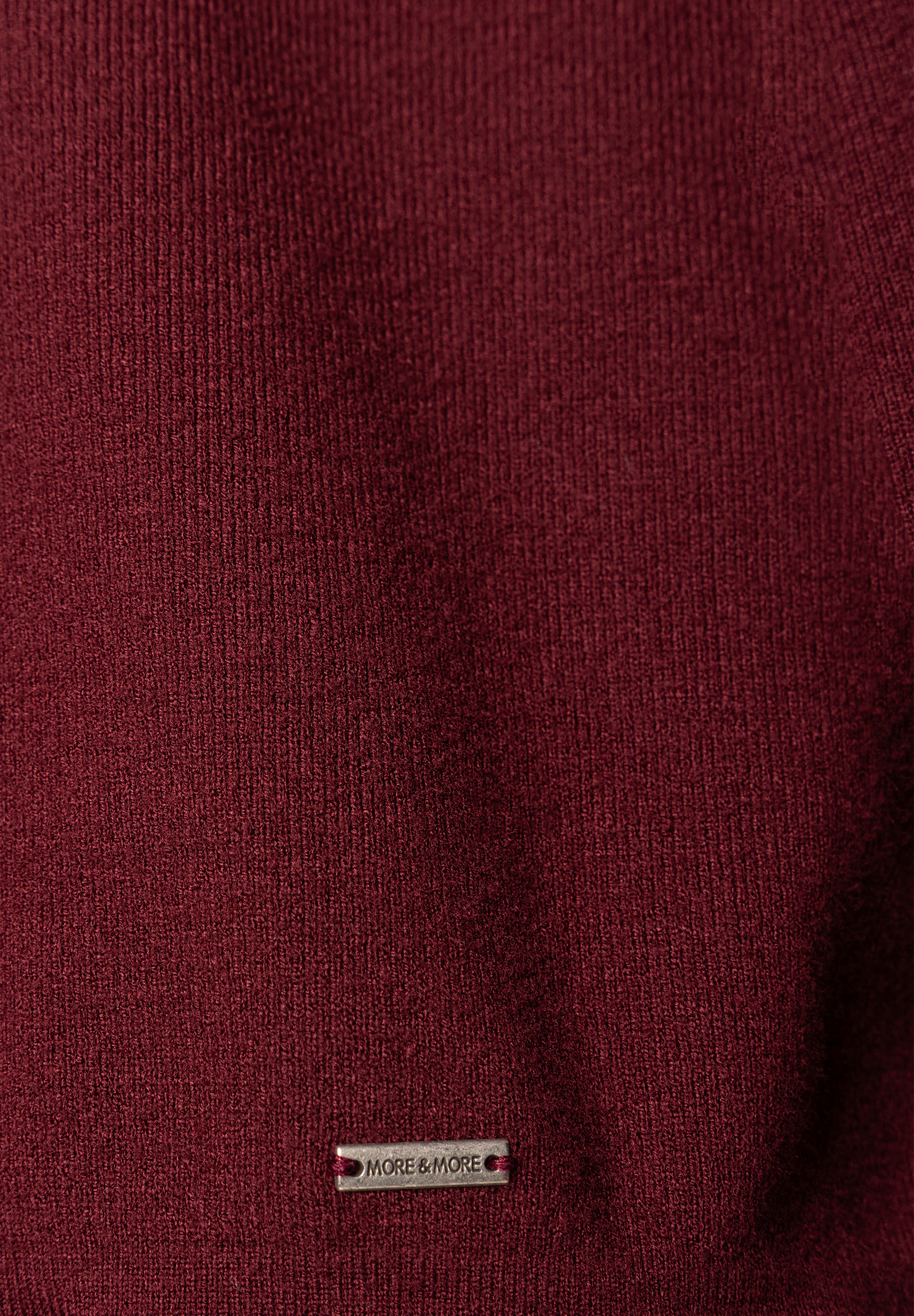 Nahaufnahme eines MORE & MORE Pullovers in Dunkelrot mit feinem Strickmuster und einem kleinen, silbernen Markenlabel.