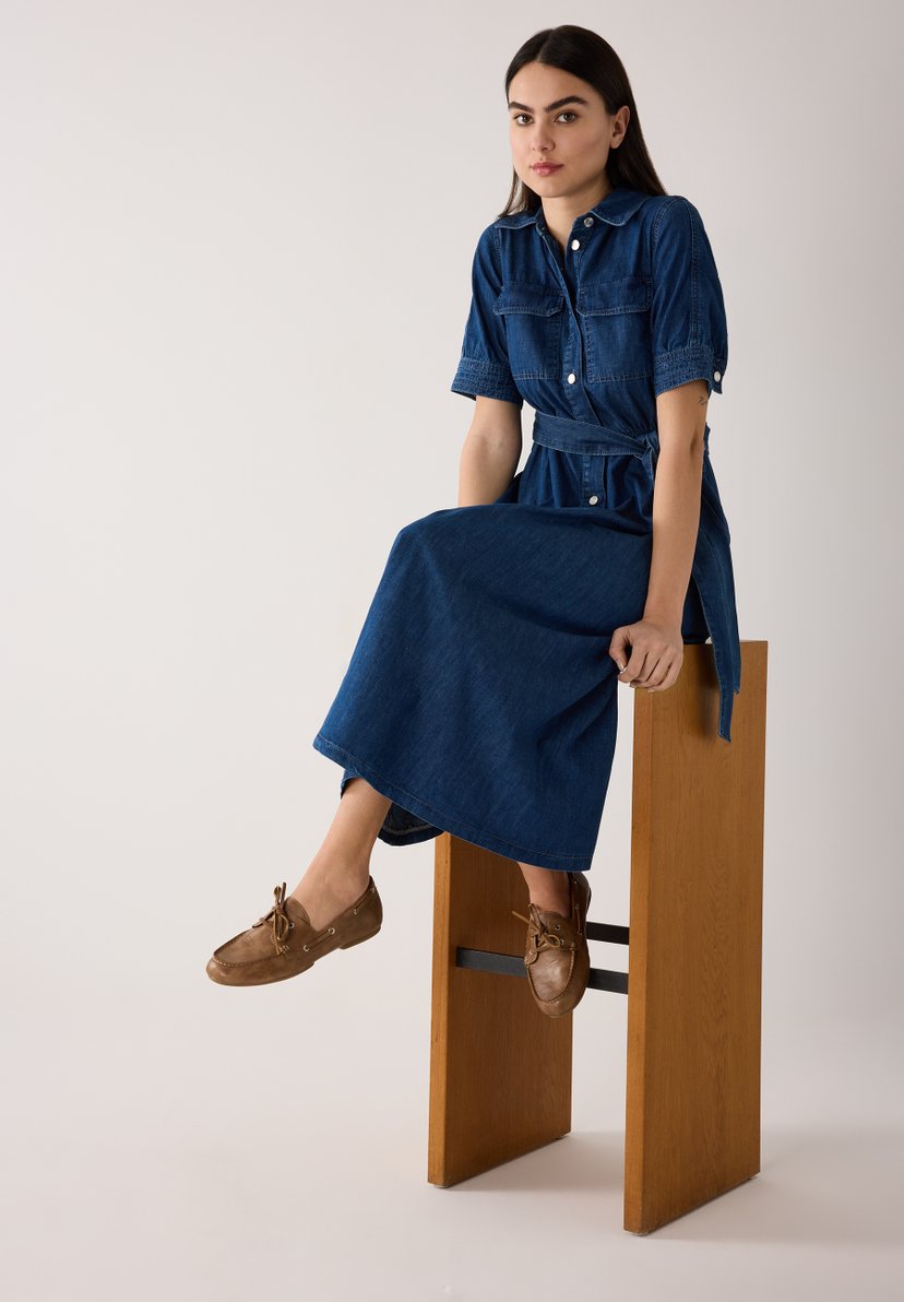 Eine Frau im MORE & MORE Jeanskleid sitzt auf einem Barhocker. Sie trägt braune Schuhe. Das Kleid hat einen Gürtel und kurze Ärmel. Eine Frau im MORE & MORE Jeanskleid sitzt auf einem Barhocker. Sie trägt braune Schuhe. Das Kleid hat einen Gürtel und kurze Ärmel.