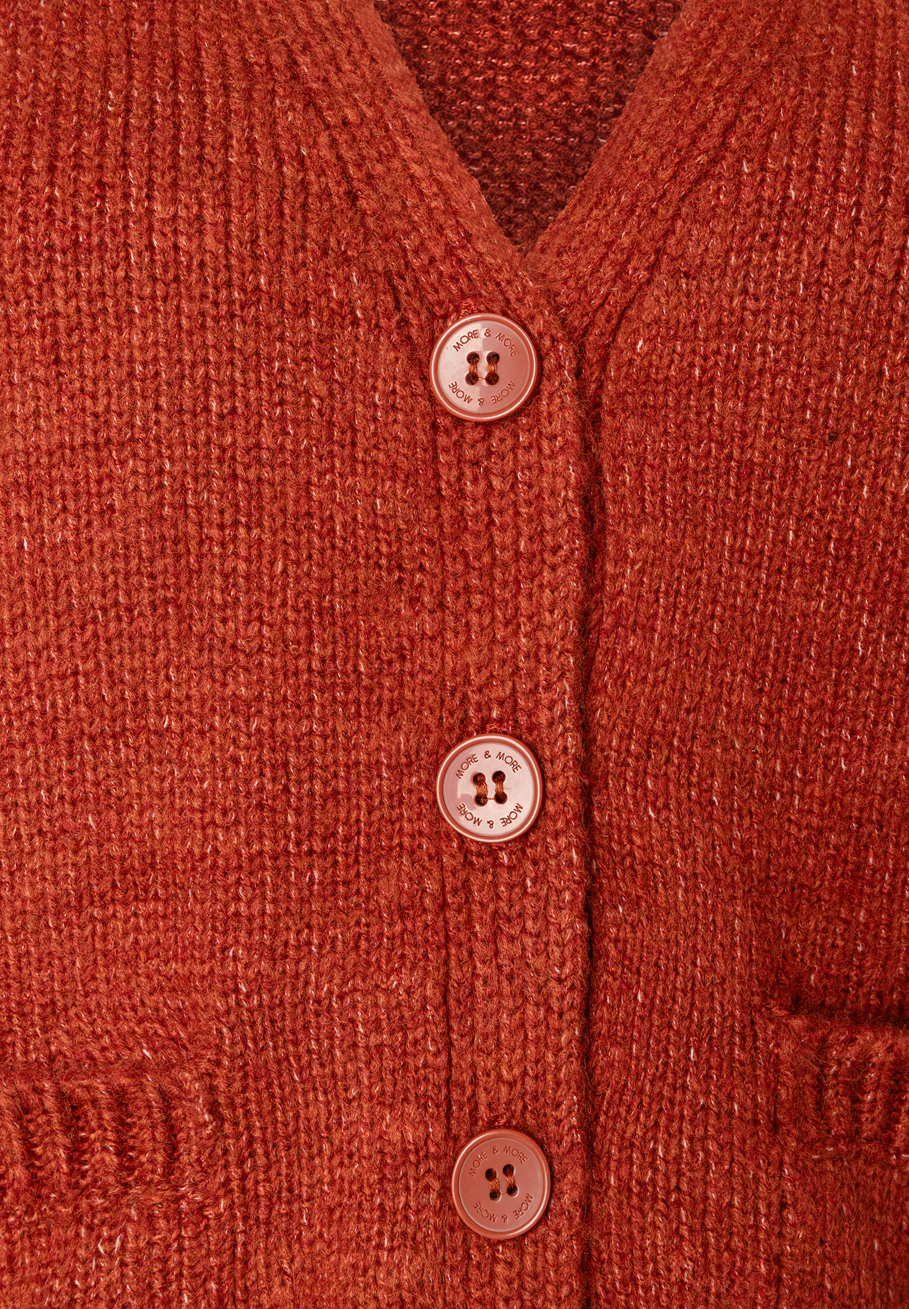 Nahaufnahme einer gestrickten, orangefarbenen MORE & MORE Strickjacke mit Knöpfen. Nahaufnahme einer gestrickten, orangefarbenen MORE & MORE Strickjacke mit Knöpfen.