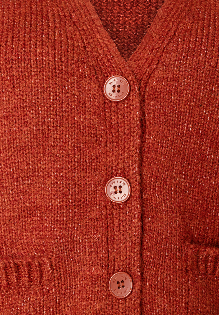 Nahaufnahme einer gestrickten, orangefarbenen MORE & MORE Strickjacke mit Knöpfen. Nahaufnahme einer gestrickten, orangefarbenen MORE & MORE Strickjacke mit Knöpfen.