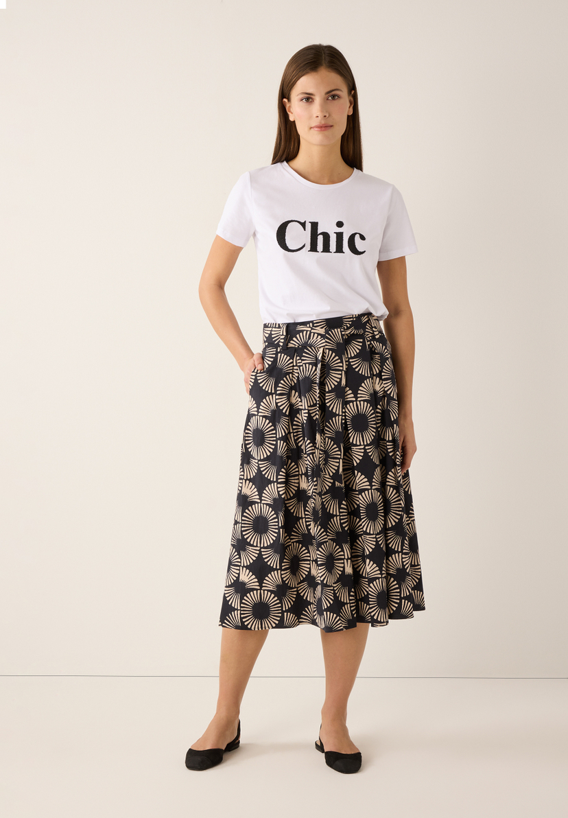Eine Frau im MORE & MORE T-Shirt mit dem Aufdruck "Chic", kombiniert mit einem gemusterten Rock. Eine Frau im MORE & MORE T-Shirt mit dem Aufdruck "Chic", kombiniert mit einem gemusterten Rock.