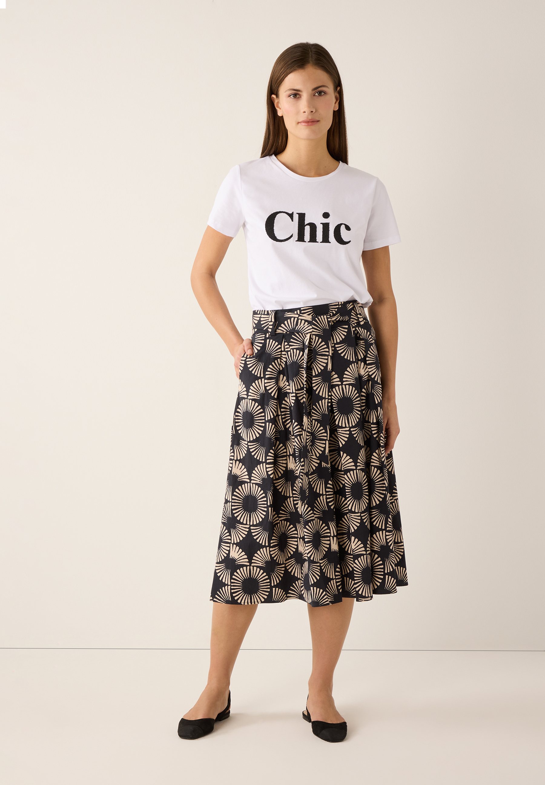 Eine Frau im MORE & MORE T-Shirt mit dem Aufdruck "Chic", kombiniert mit einem gemusterten Rock. Eine Frau im MORE & MORE T-Shirt mit dem Aufdruck "Chic", kombiniert mit einem gemusterten Rock.