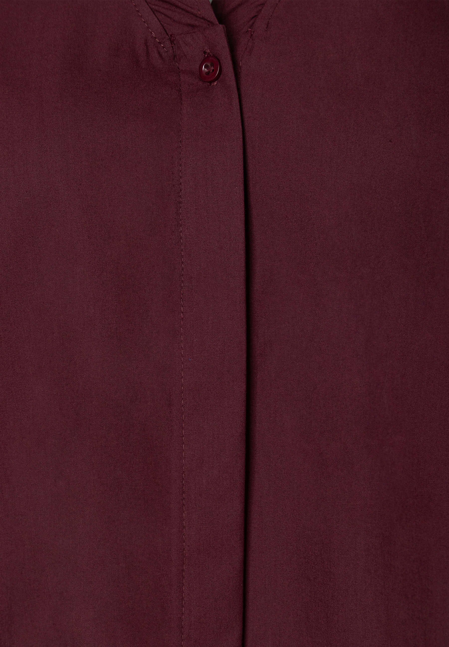 MORE & MORE Bluse in Bordeauxrot. Detailaufnahme der Knopfleiste mit einem einzelnen, runden, dunkelroten Knopf.