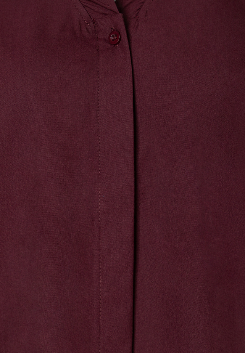 MORE & MORE Bluse in Bordeauxrot. Detailaufnahme der Knopfleiste mit einem einzelnen, runden, dunkelroten Knopf. MORE & MORE Bluse in Bordeauxrot. Detailaufnahme der Knopfleiste mit einem einzelnen, runden, dunkelroten Knopf.