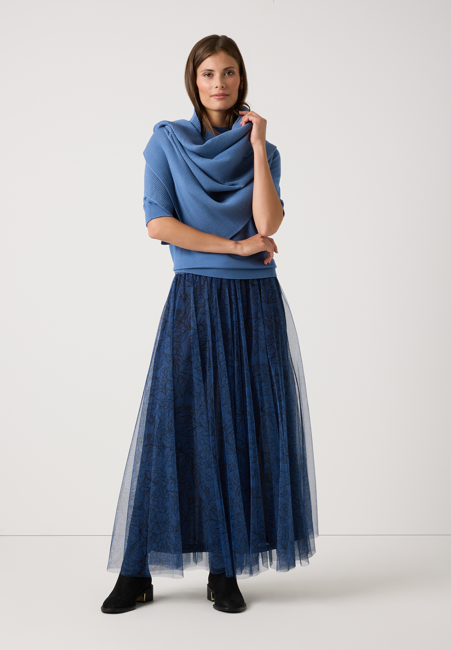 Eine Frau trägt einen langen, blauen MORE & MORE Rock aus Mesh. Der Rock hat ein florales Muster. Eine Frau trägt einen langen, blauen MORE & MORE Rock aus Mesh. Der Rock hat ein florales Muster.