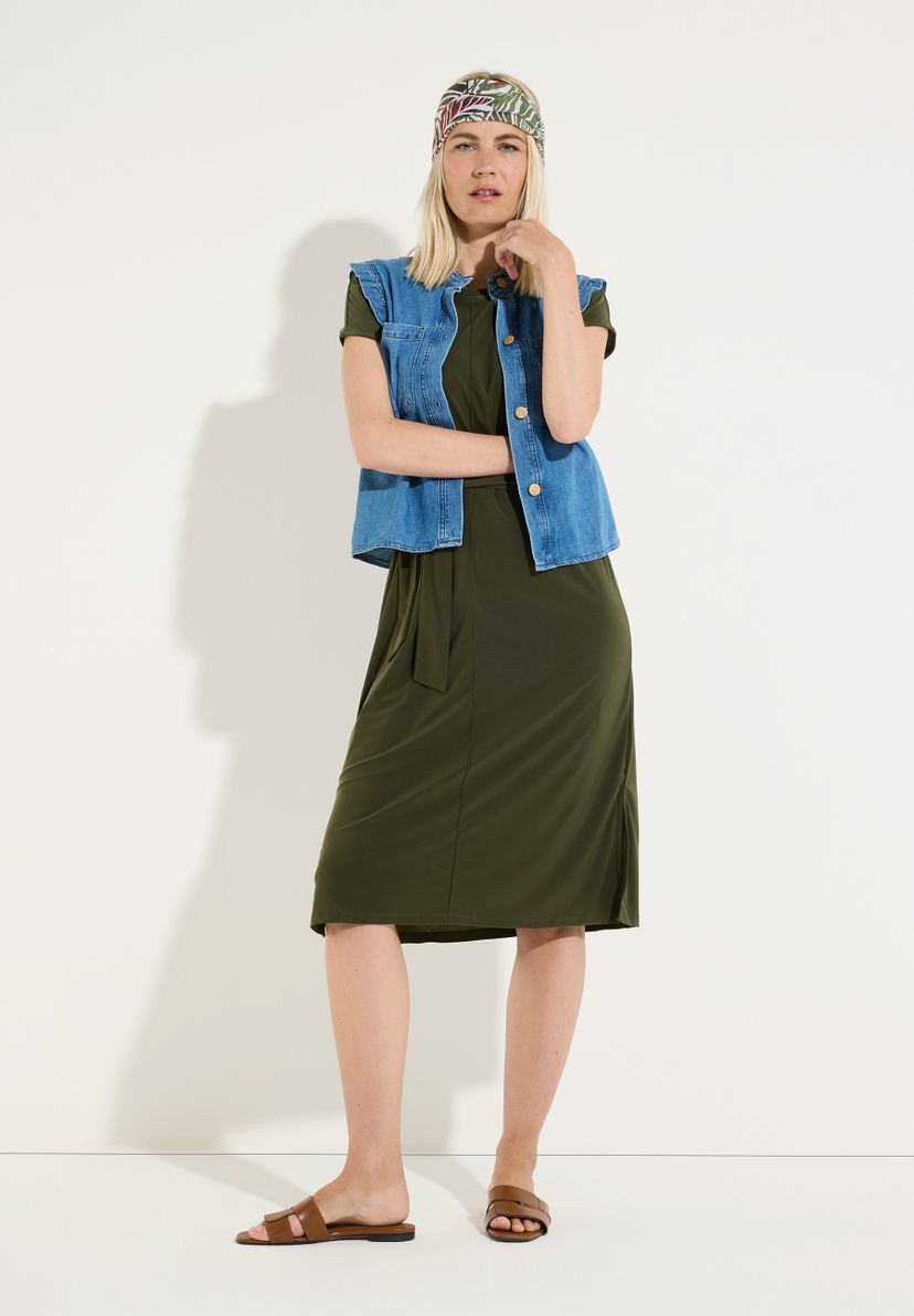MORE & MORE Midikleid in Dunkelgrün mit bindeband und kurzem Arm. Eine blonde Frau trägt dazu eine Jeansweste und braune Sandalen. MORE & MORE Midikleid in Dunkelgrün mit bindeband und kurzem Arm. Eine blonde Frau trägt dazu eine Jeansweste und braune Sandalen.