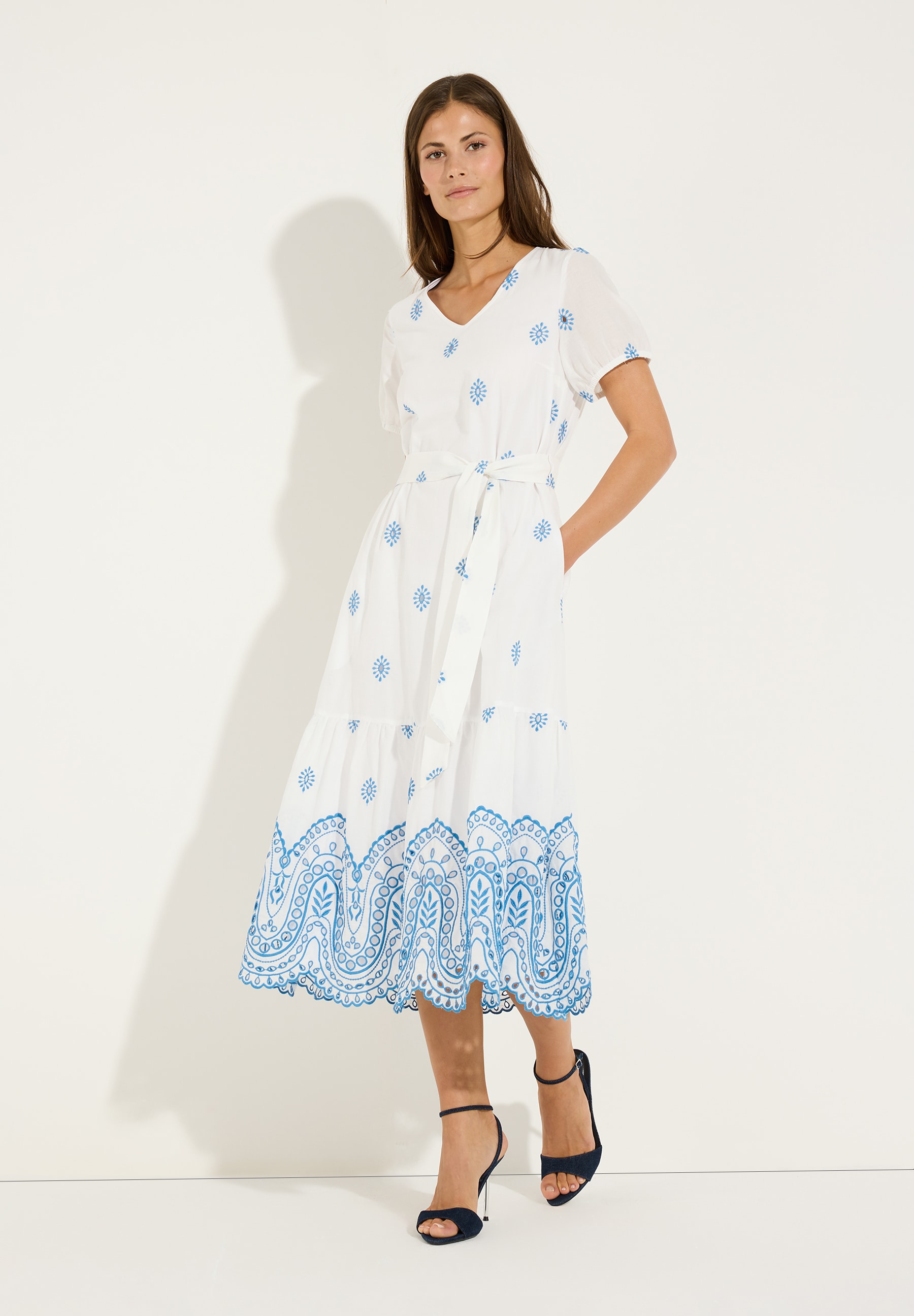 MORE & MORE Oberteil: Weißes Kleid mit blauen Blumenstickereien und Schnürung, kombiniert mit dunklen Absätzen.