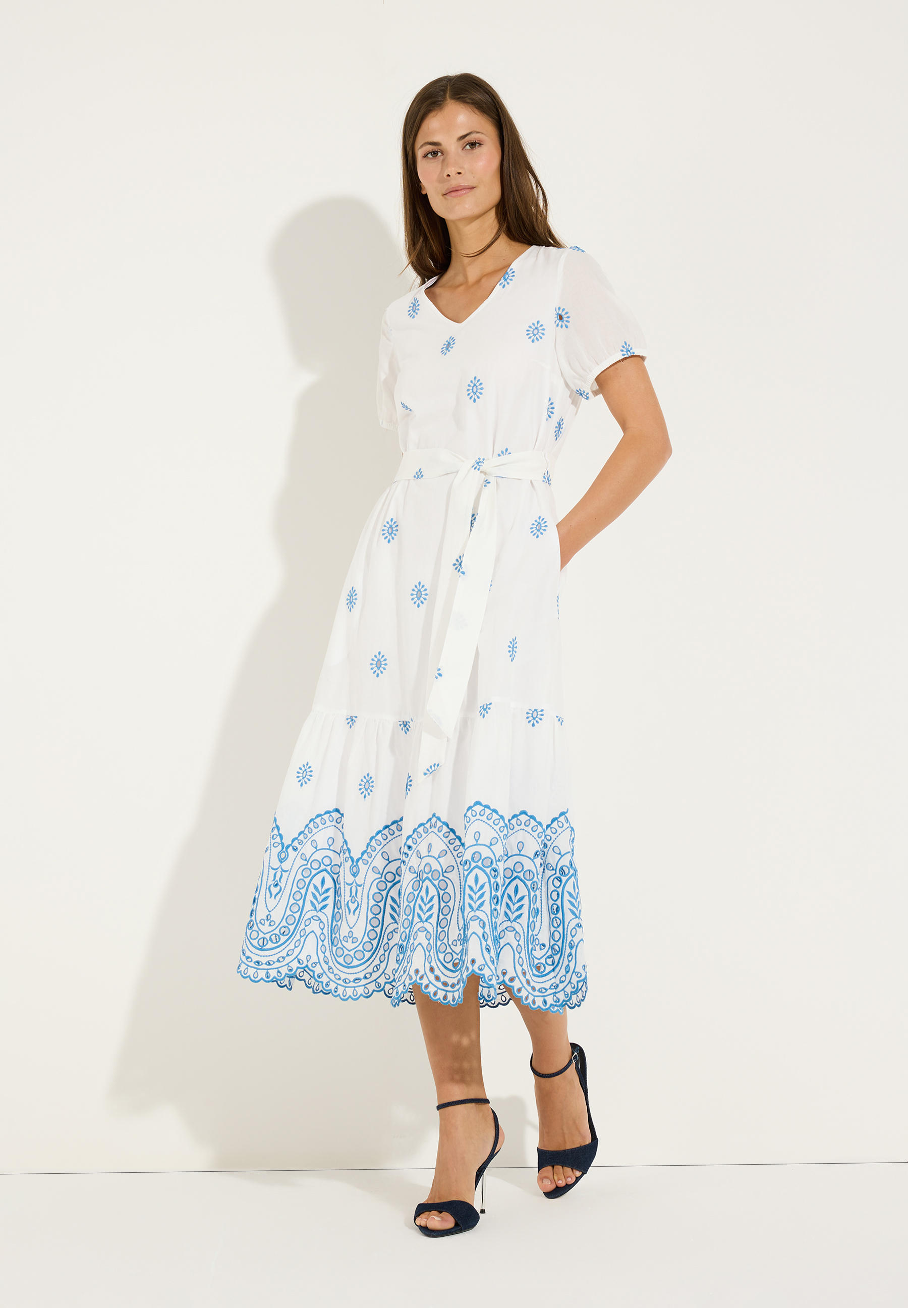 MORE & MORE Oberteil: Weißes Kleid mit blauen Blumenstickereien und Schnürung, kombiniert mit dunklen Absätzen.