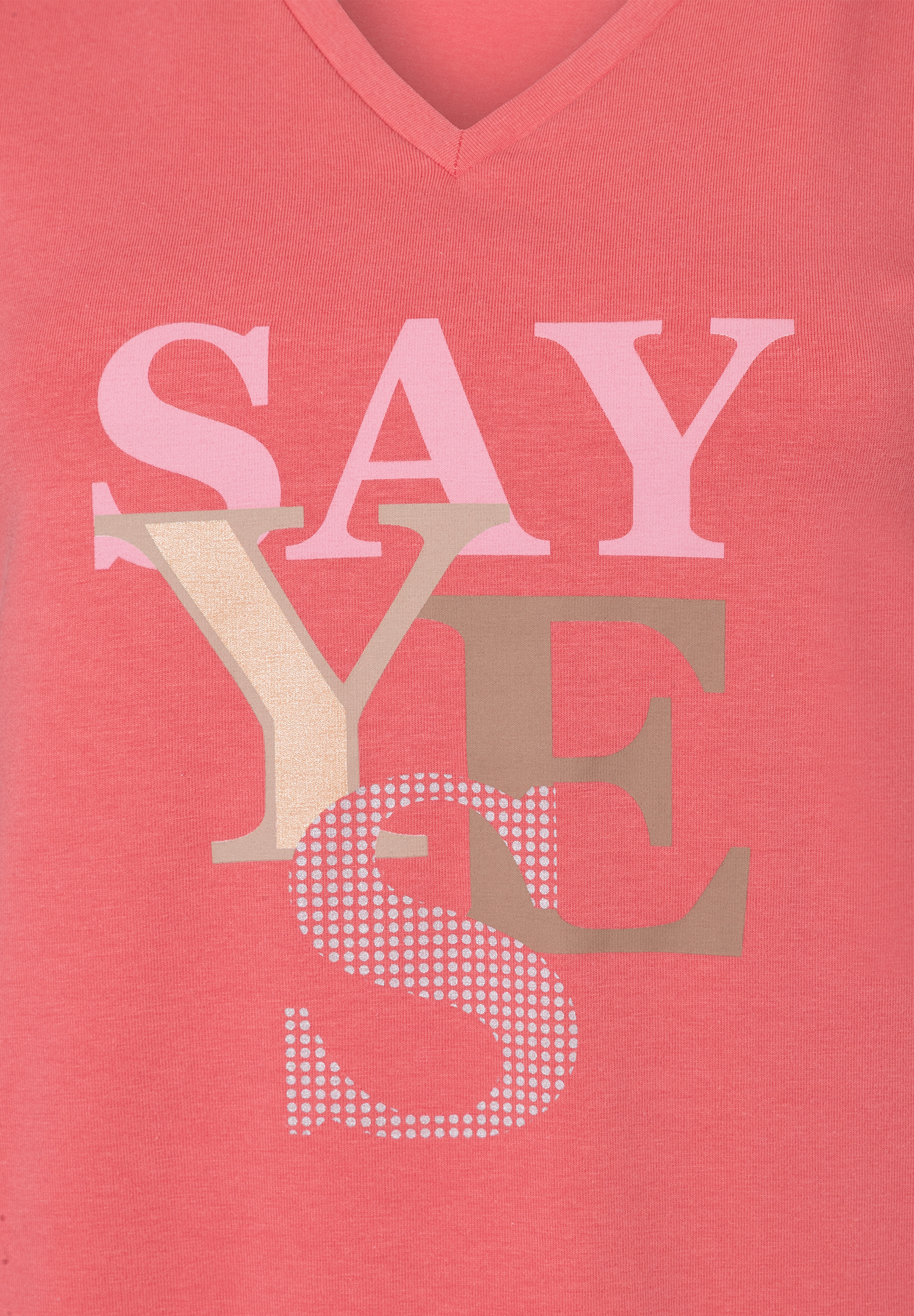 Nahaufnahme eines korallfarbenen MORE & MORE T-Shirts mit V-Ausschnitt und dem Aufdruck „SAY YES“ in Rosa- und Beigetönen. Nahaufnahme eines korallfarbenen MORE & MORE T-Shirts mit V-Ausschnitt und dem Aufdruck „SAY YES“ in Rosa- und Beigetönen.