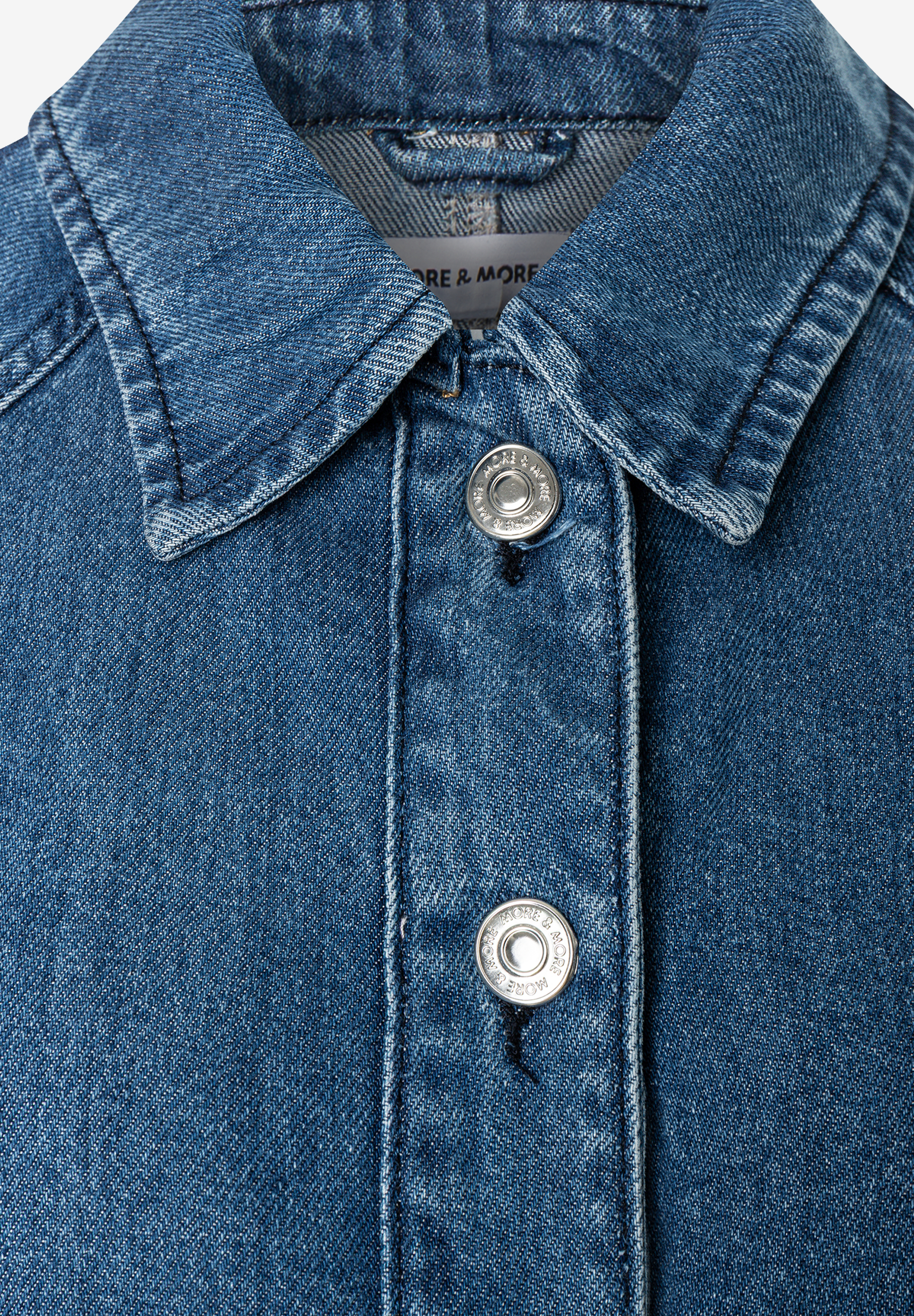 MORE & MORE Jeansjacke aus Denim. Nahaufnahme des oberen Knopfverschlusses mit dem Markenlogo auf den Knöpfen. MORE & MORE Jeansjacke aus Denim. Nahaufnahme des oberen Knopfverschlusses mit dem Markenlogo auf den Knöpfen.