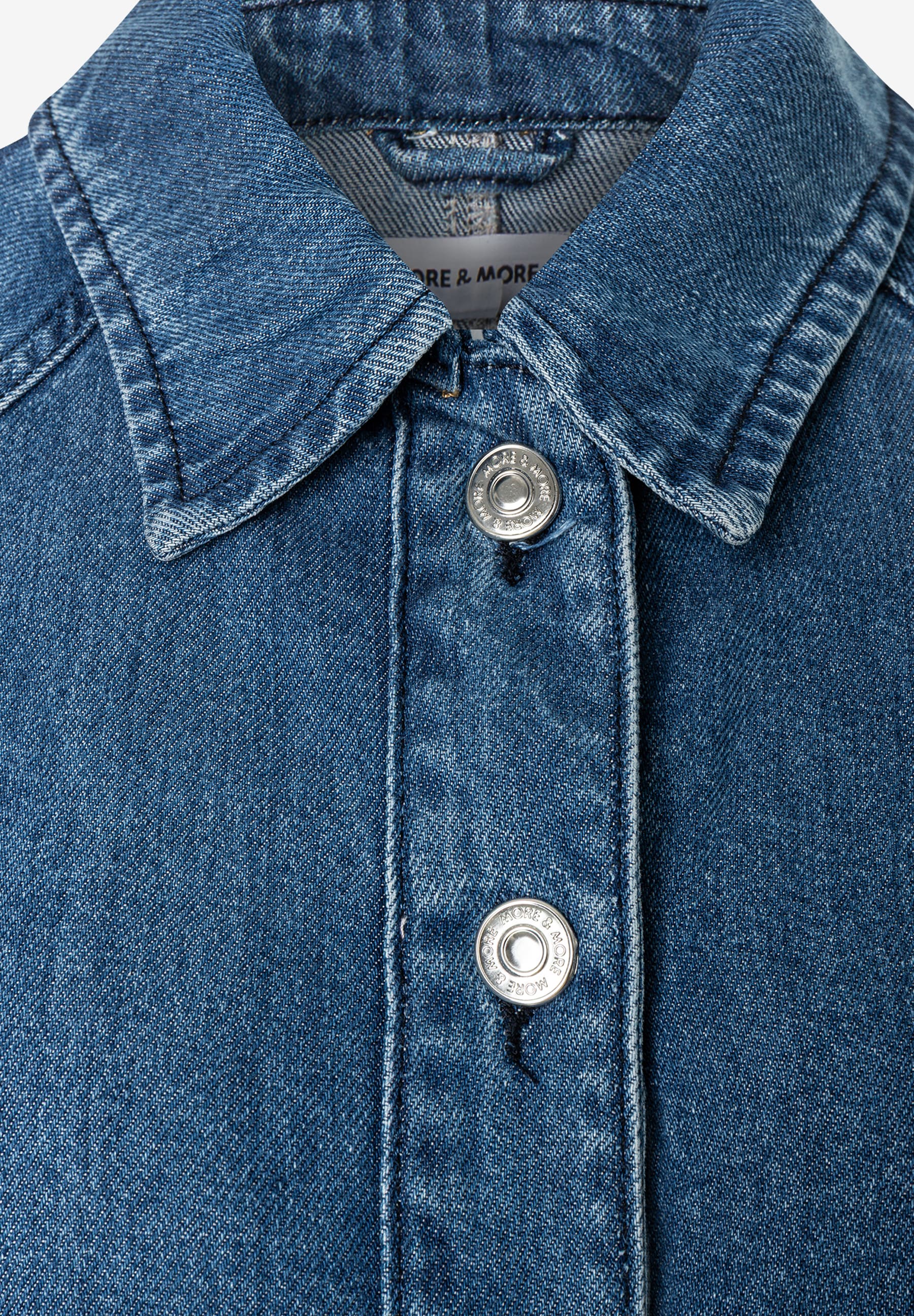 MORE & MORE Jeansjacke aus Denim. Nahaufnahme des oberen Knopfverschlusses mit dem Markenlogo auf den Knöpfen. MORE & MORE Jeansjacke aus Denim. Nahaufnahme des oberen Knopfverschlusses mit dem Markenlogo auf den Knöpfen.