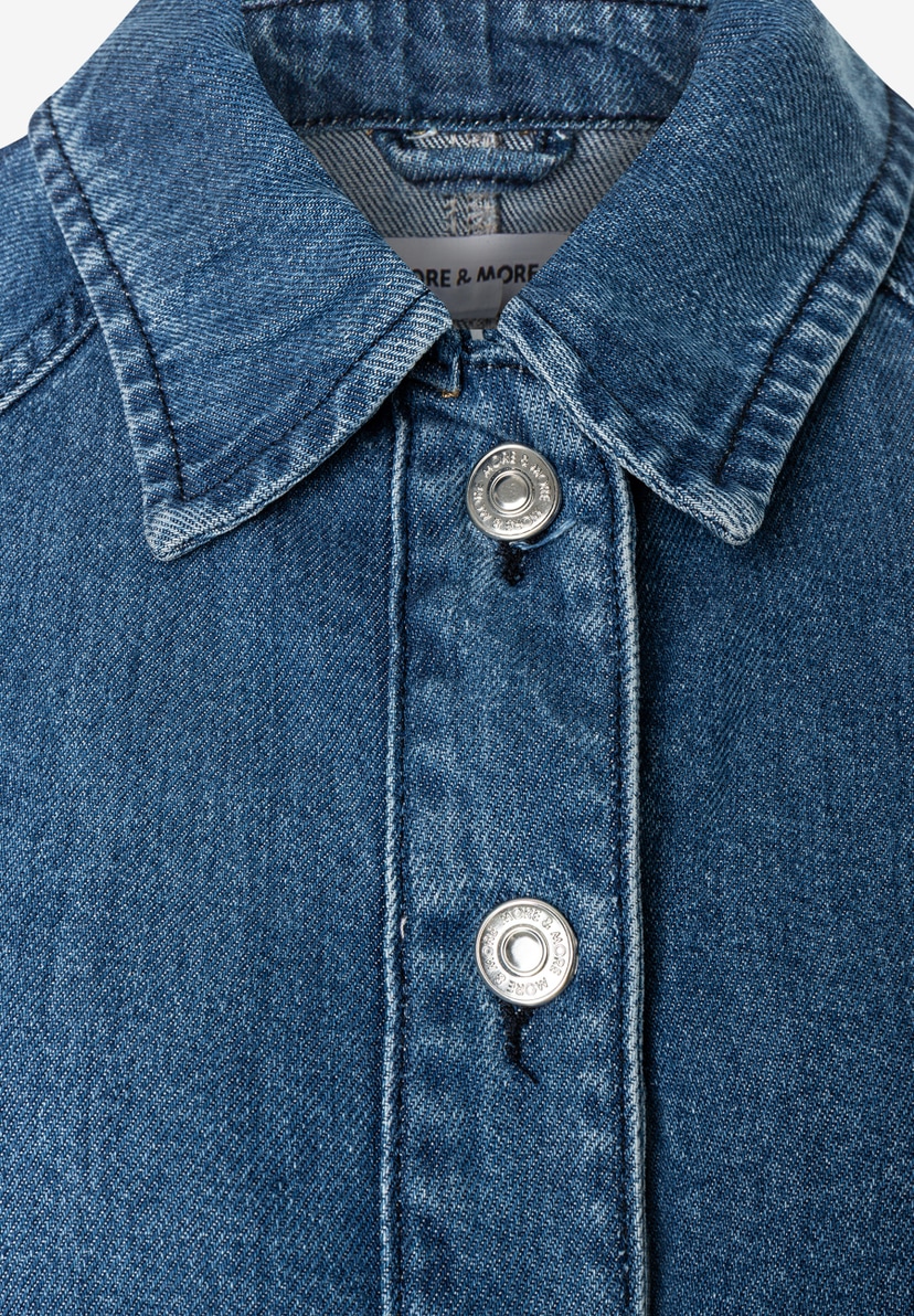 MORE & MORE Jeansjacke aus Denim. Nahaufnahme des oberen Knopfverschlusses mit dem Markenlogo auf den Knöpfen. MORE & MORE Jeansjacke aus Denim. Nahaufnahme des oberen Knopfverschlusses mit dem Markenlogo auf den Knöpfen.