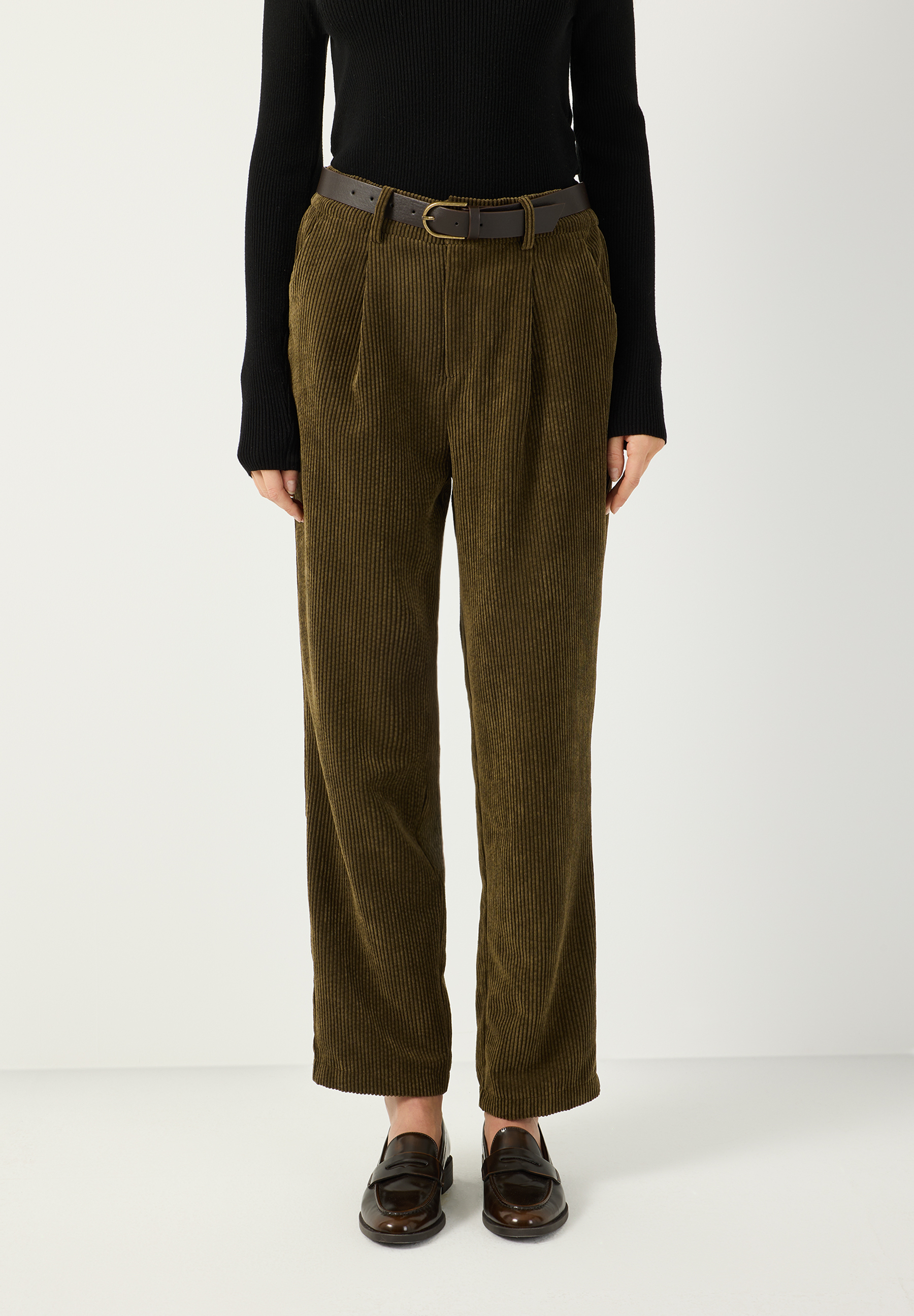 MORE & MORE Cordhose in Khaki mit Bundfalten und Ledergürtel, kombiniert mit schwarzem Langarmshirt und Loafers.