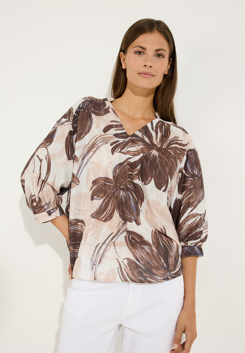 MORE & MORE Bluse mit V-Ausschnitt, 3/4-Ärmeln und braunem Blumenmuster, kombiniert mit weißer Hose. MORE & MORE Bluse mit V-Ausschnitt, 3/4-Ärmeln und braunem Blumenmuster, kombiniert mit weißer Hose.