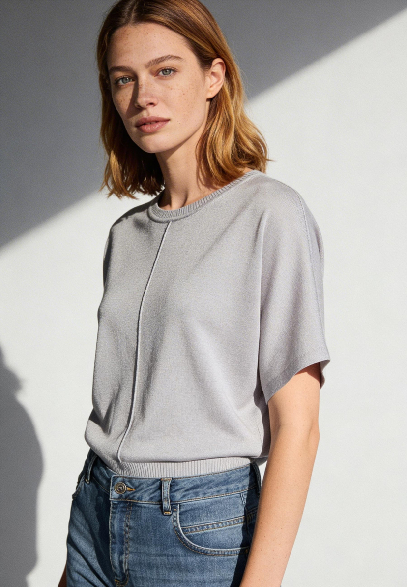 AI generated - Eine Frau mit Sommersprossen trägt ein MORE & MORE Strickoberteil und Jeans vor einer weißen Wand. AI generated - Eine Frau mit Sommersprossen trägt ein MORE & MORE Strickoberteil und Jeans vor einer weißen Wand.