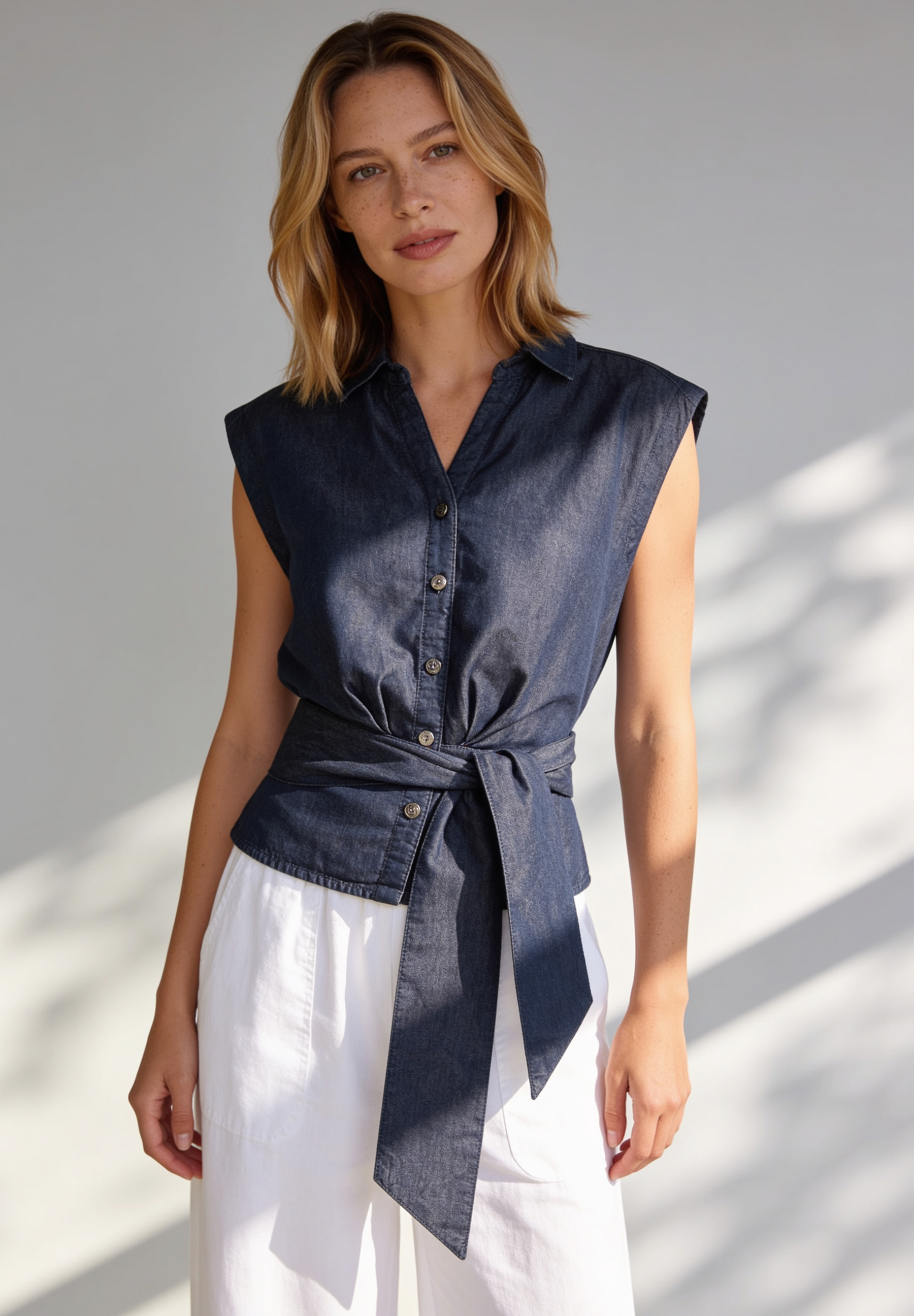 AI generated - MORE & MORE Damenbluse aus Denim mit kurzer Knopfleiste und Gürtel. Eine Blondine posiert vor weißem Hintergrund. AI generated - MORE & MORE Damenbluse aus Denim mit kurzer Knopfleiste und Gürtel. Eine Blondine posiert vor weißem Hintergrund.