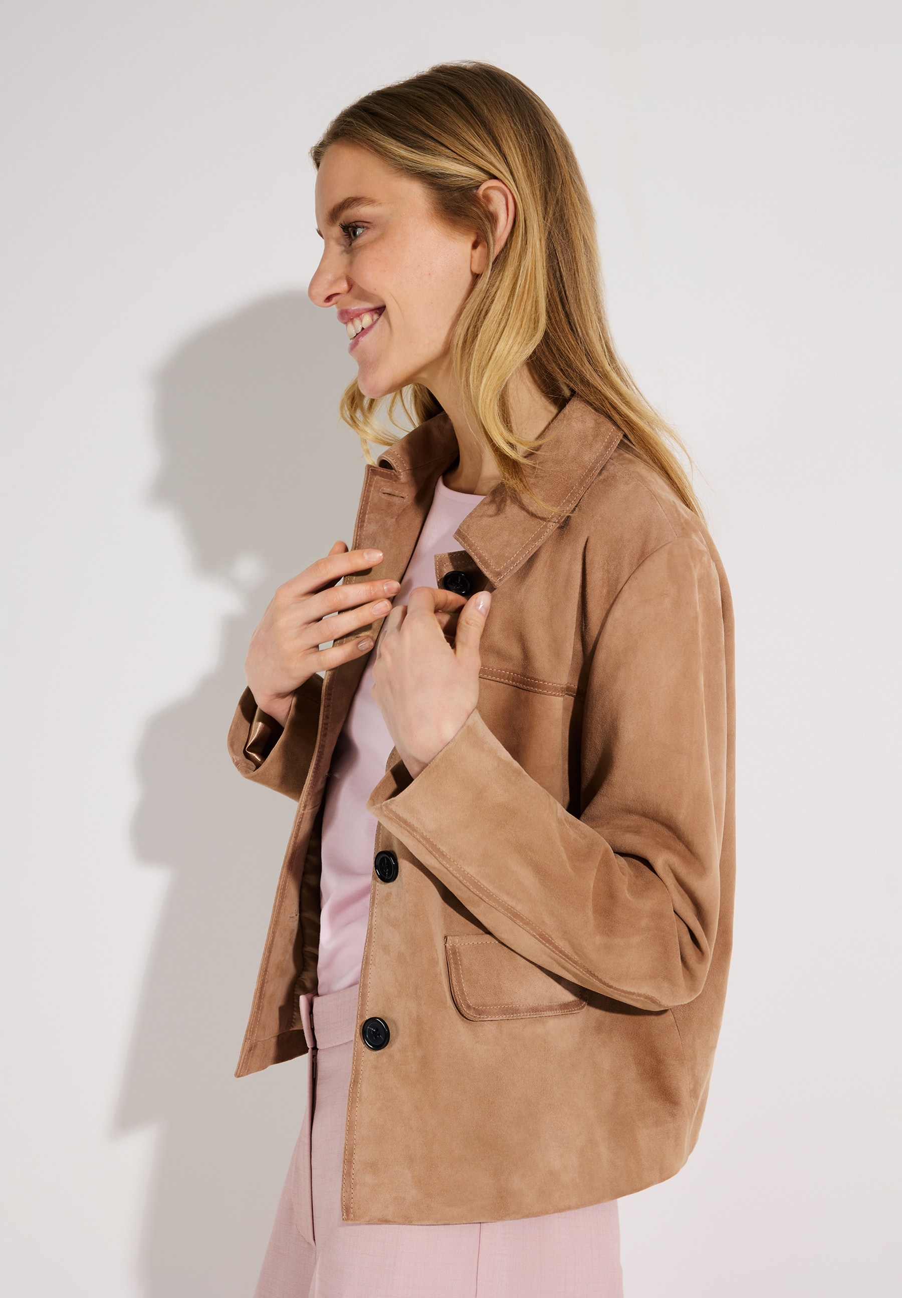 Eine lächelnde Frau trägt eine MORE & MORE Wildlederjacke, mit Knöpfen und Taschen. Eine lächelnde Frau trägt eine MORE & MORE Wildlederjacke, mit Knöpfen und Taschen.