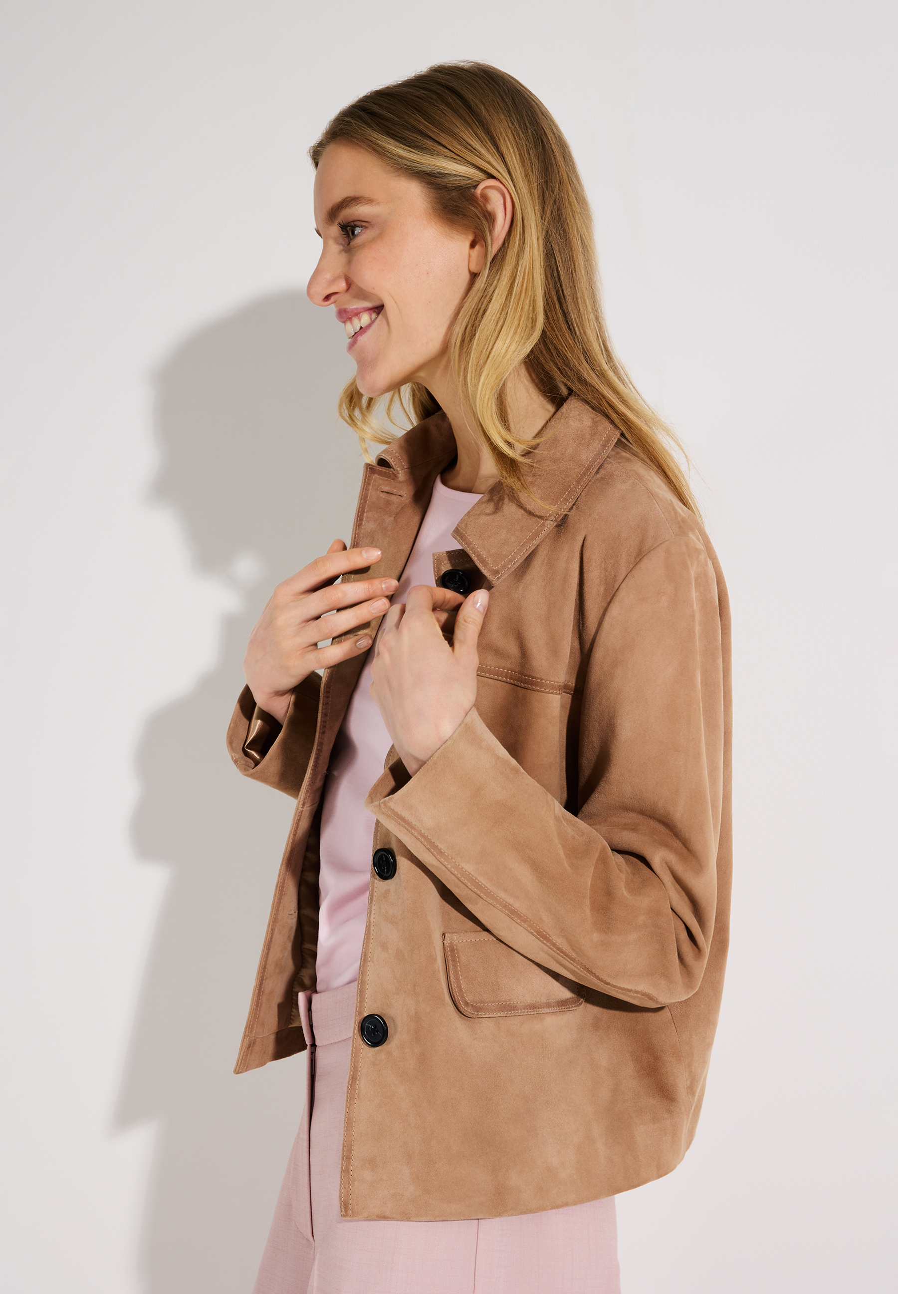 Eine lächelnde Frau trägt eine MORE & MORE Wildlederjacke, mit Knöpfen und Taschen. Eine lächelnde Frau trägt eine MORE & MORE Wildlederjacke, mit Knöpfen und Taschen.