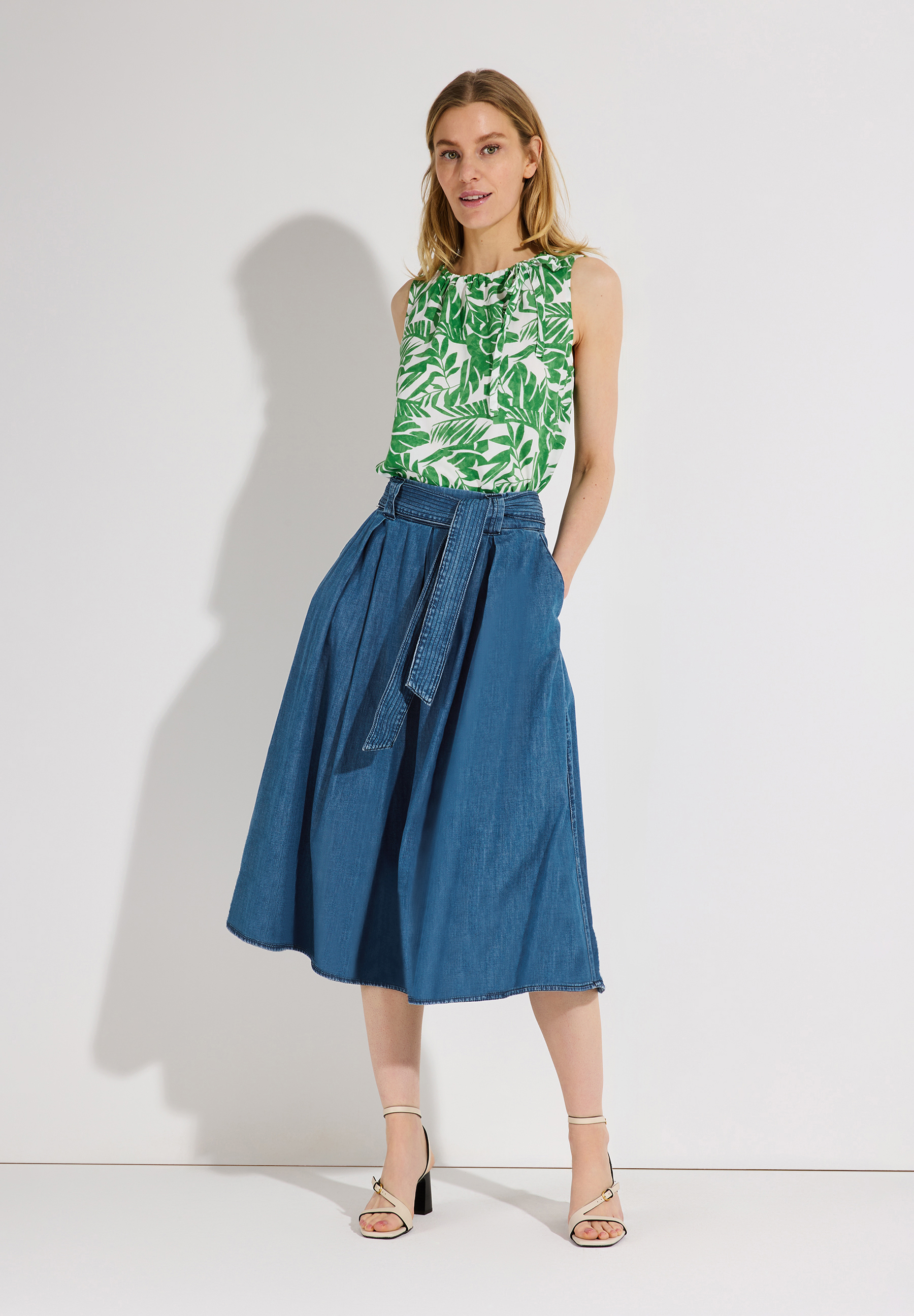 Eine Frau mit einem MORE & MORE Rock und einem grünen Oberteil vor weißem Hintergrund.