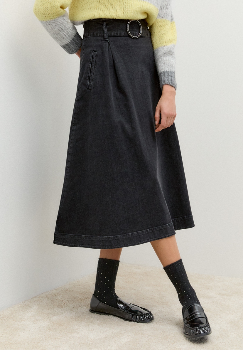 Eine Person trägt einen MORE & MORE Jeansrock. Der Rock ist knielang und wird mit einem Gürtel geschlossen. Eine Person trägt einen MORE & MORE Jeansrock. Der Rock ist knielang und wird mit einem Gürtel geschlossen.