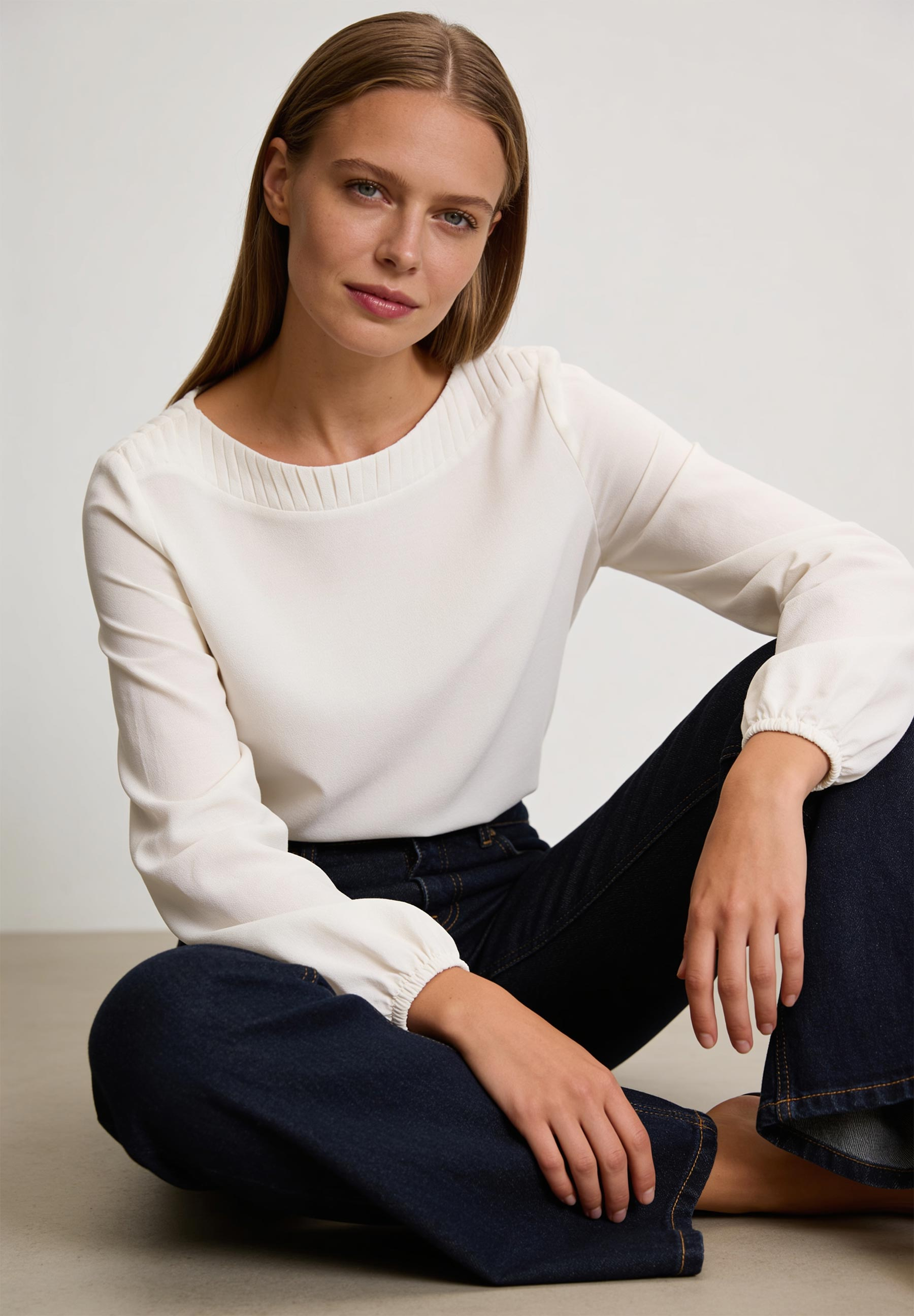 AI generated - MORE & MORE Bluse: Eine junge Frau posiert in einer cremeweißen MORE & MORE Chiffonbluse mit Rüschendetails und Jeans.