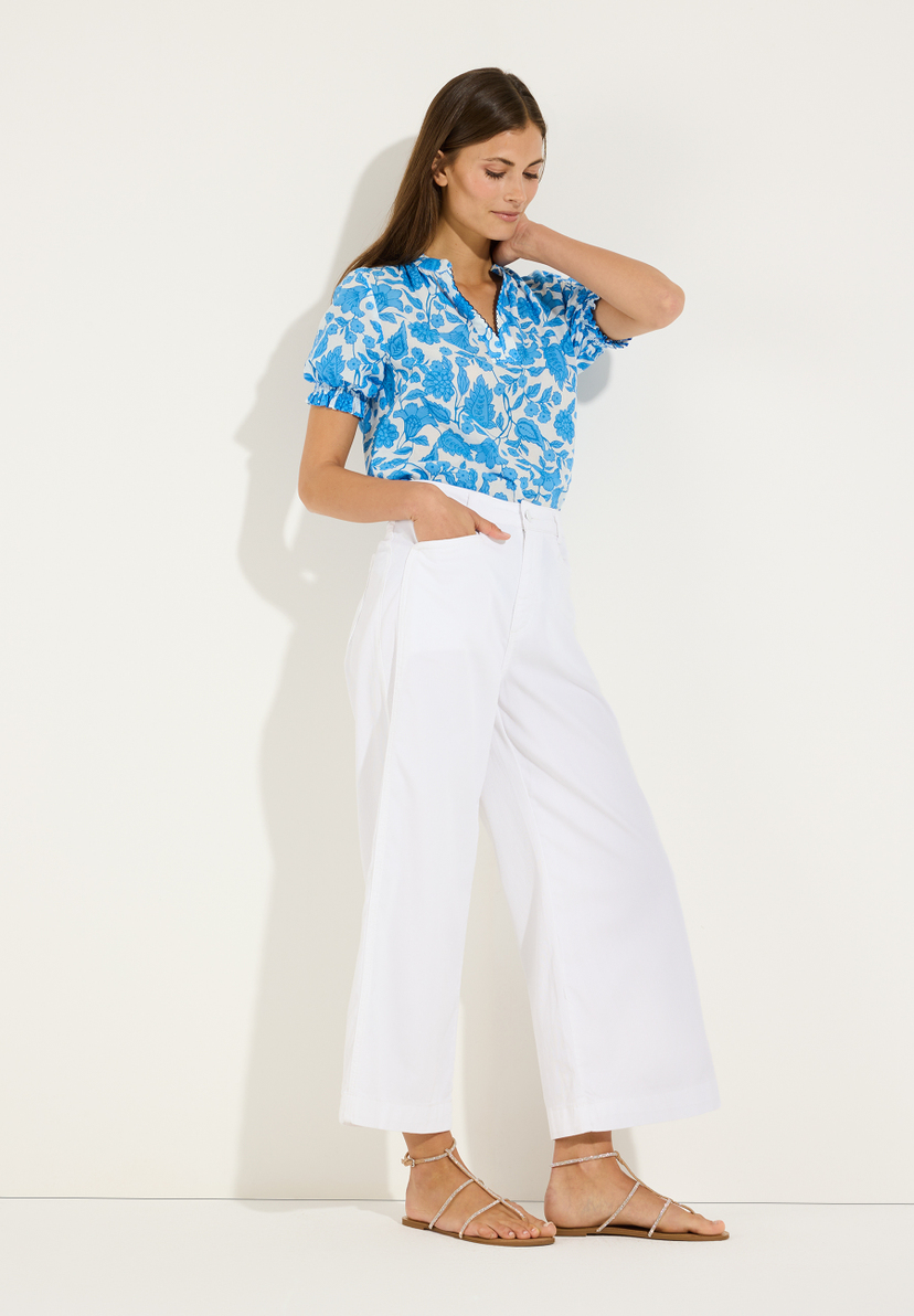 MORE & MORE Bluse: Eine junge Frau trägt eine weiße Hose & eine blau gemusterte MORE & MORE Bluse mit kurzen Ärmeln. MORE & MORE Bluse: Eine junge Frau trägt eine weiße Hose & eine blau gemusterte MORE & MORE Bluse mit kurzen Ärmeln.