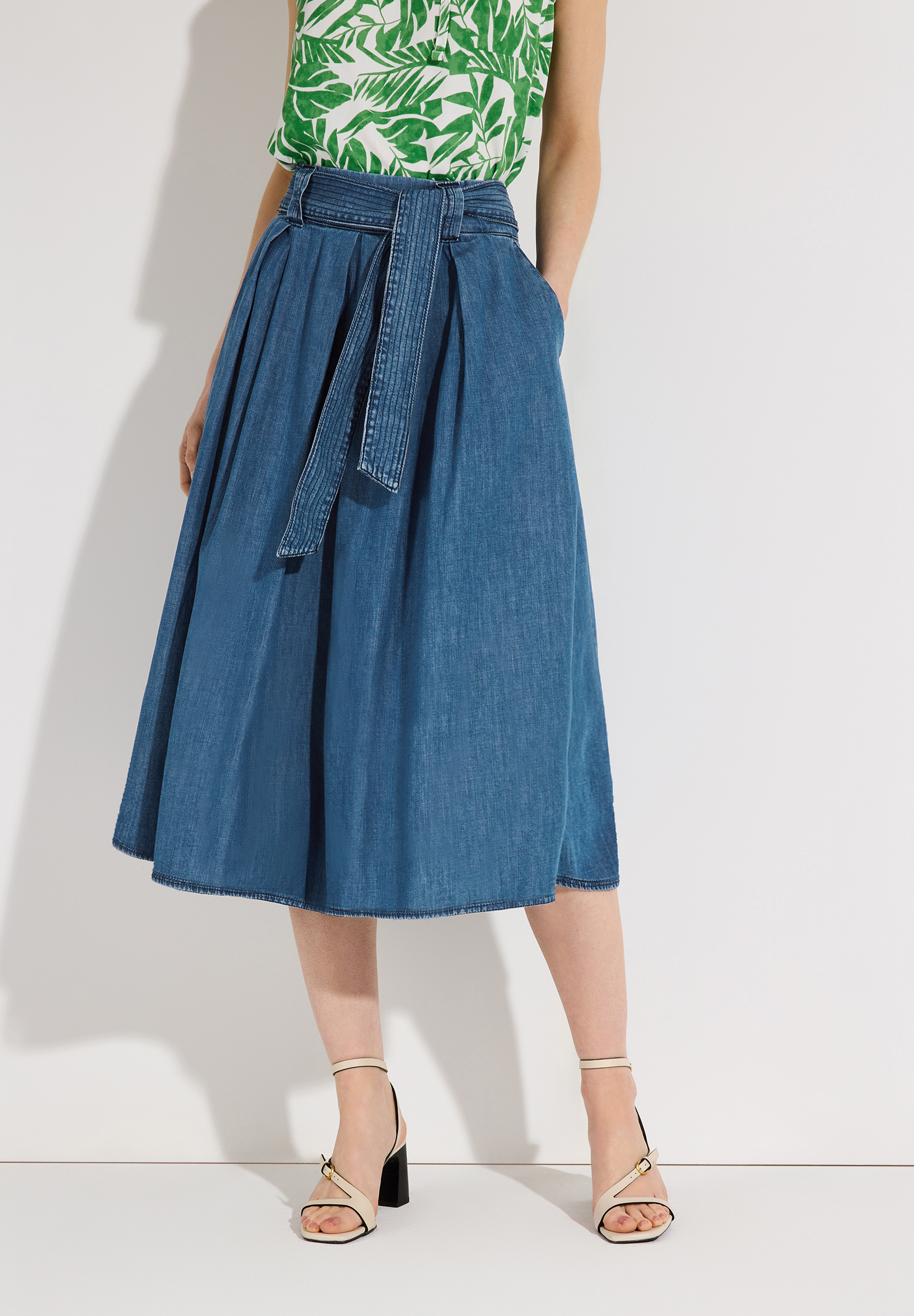 Ein Model mit einem Rock von MORE & MORE. Der Jeansrock hat eine Schleife und seitliche Eingrifftaschen.